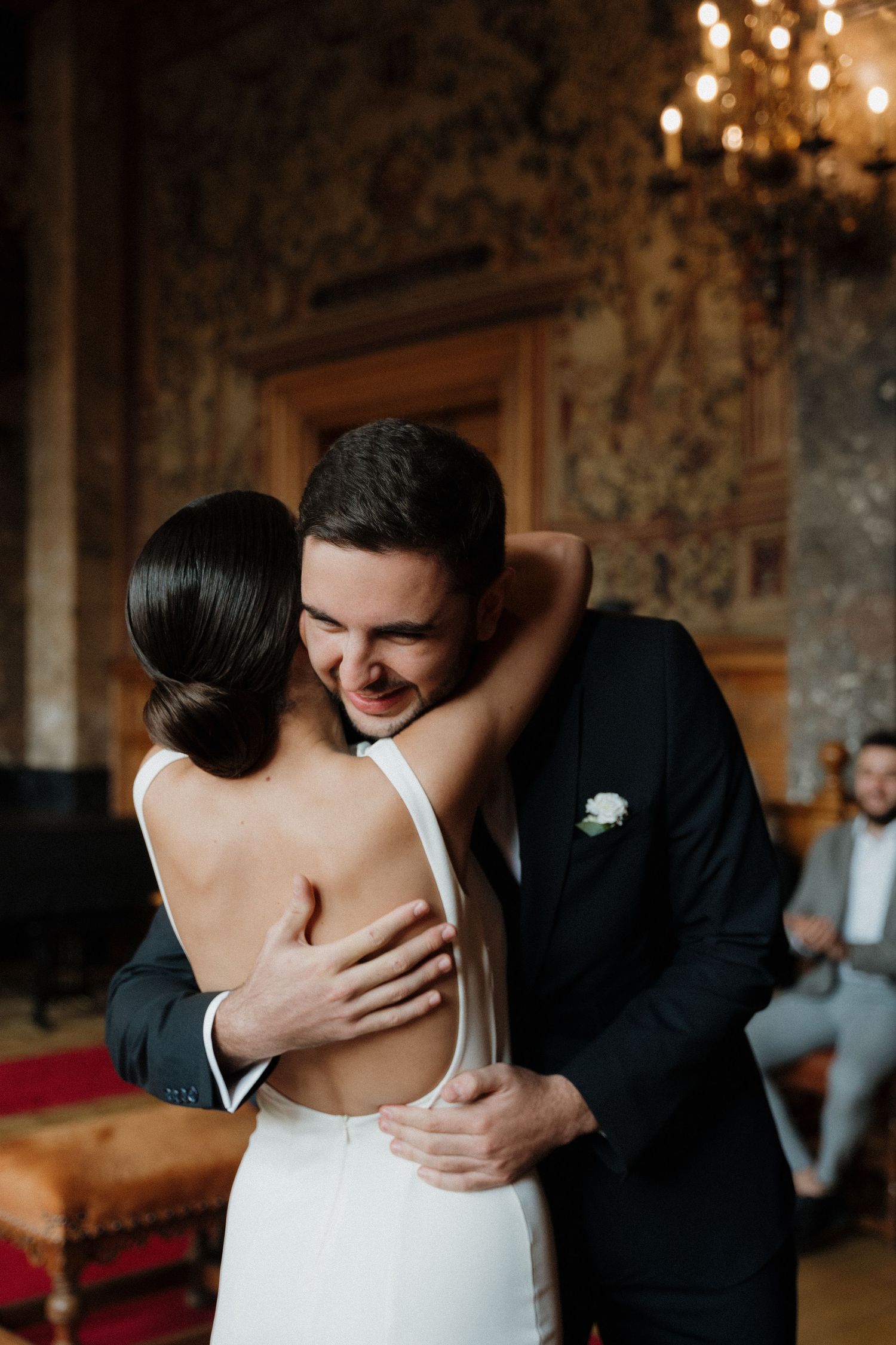 Romantic wedding photography of a newlywed couple embracing. The groom, in a beige suit, kisses the bride’s shoulder as she wears a straples