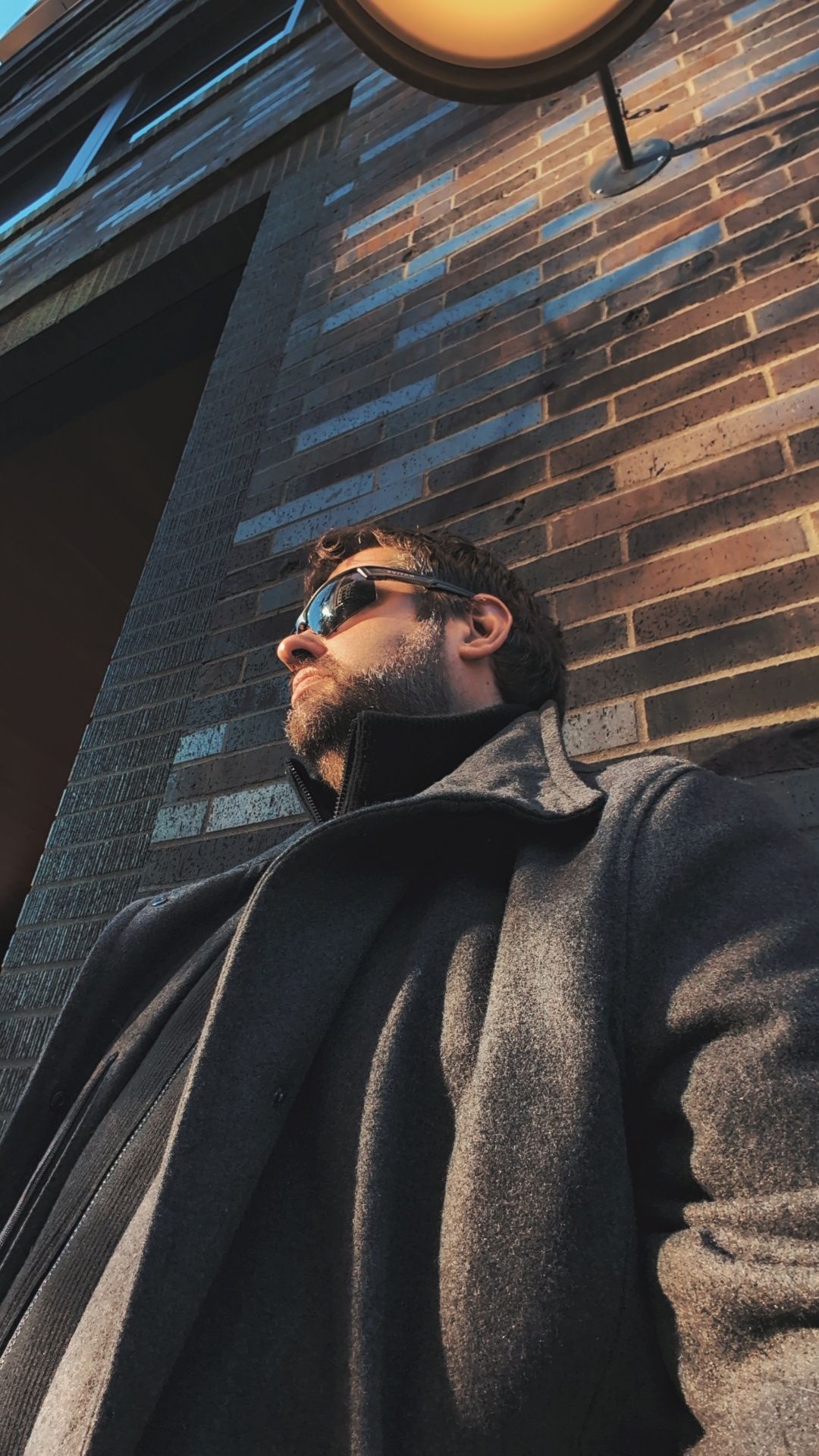DonP, Houston LGBTQ+ and lifestyle-friendly boudoir photographer, in a long coat leaning against a brick wall in warm evening light. boudoir