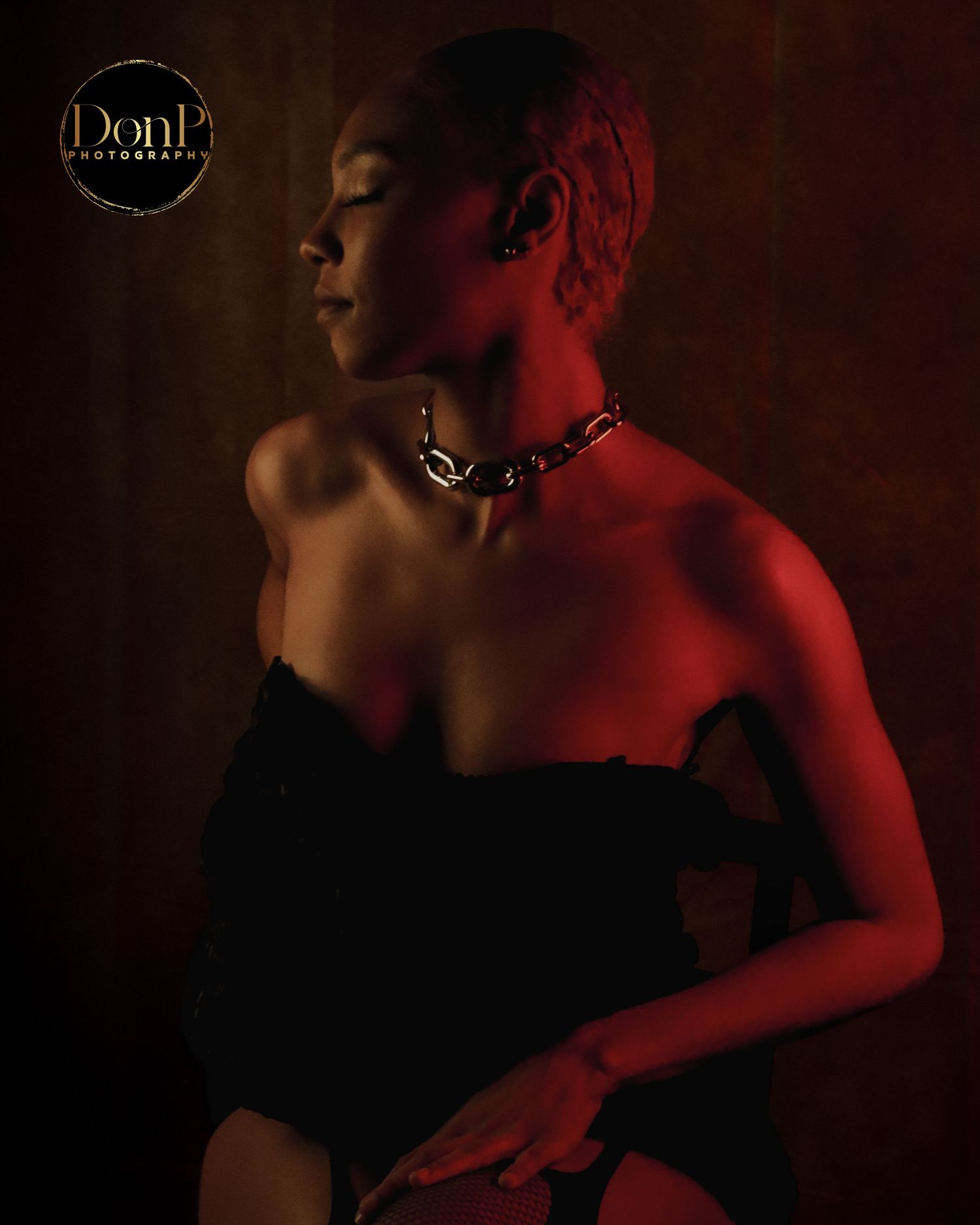 Moody boudoir photography portrait in red light, highlighting profile, posture, and sculptural elegance.