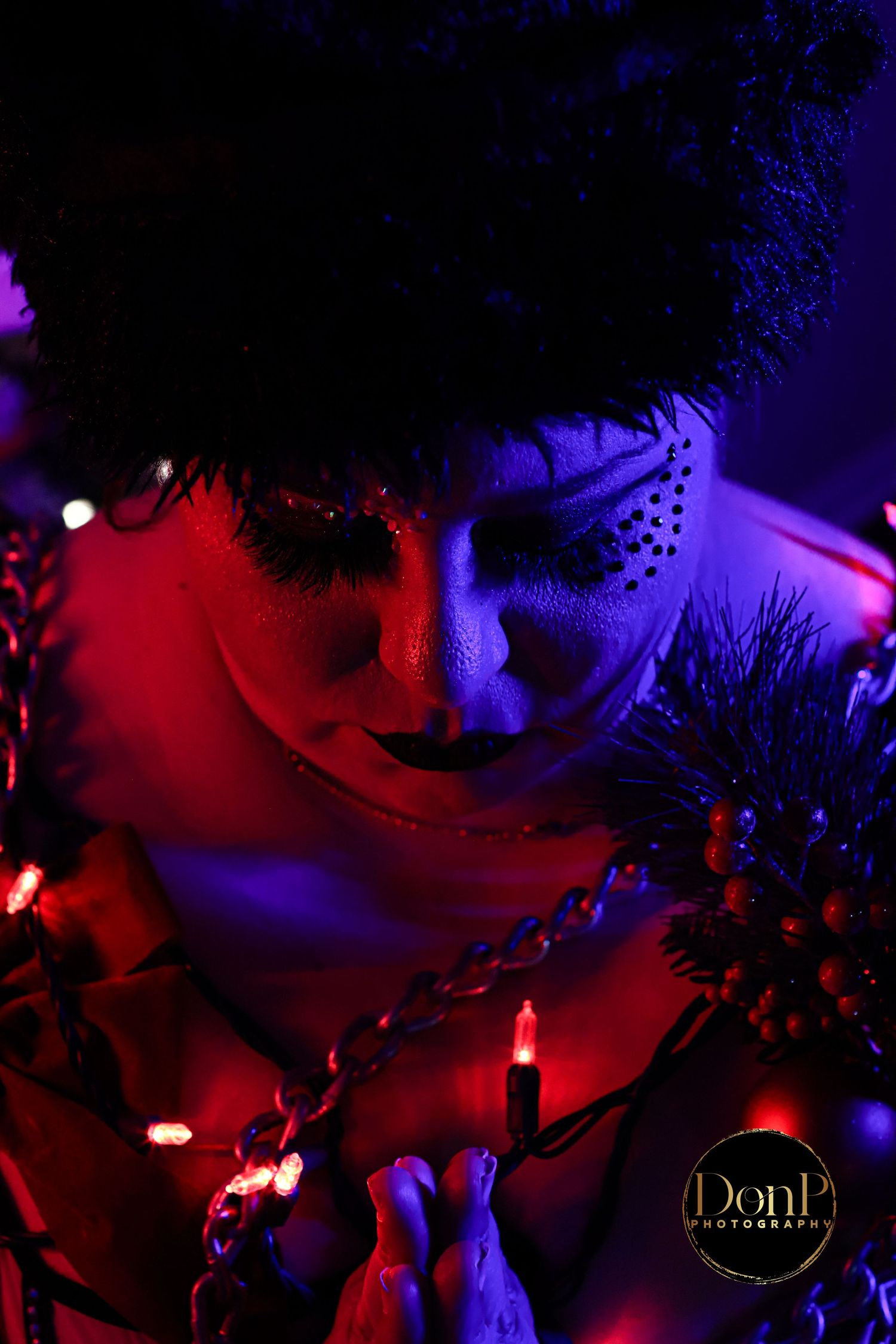 Moody, cinematic portrait of a person illuminated by red and blue light, wrapped in string lights and chains, exploring vulnerability, power