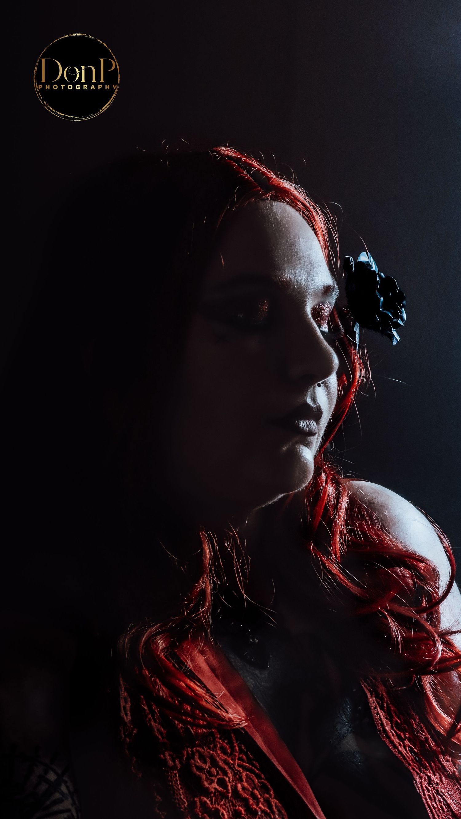 Moody boudoir photography portrait with side lighting and red hair accents, focusing on emotion, shadow, and quiet elegance.