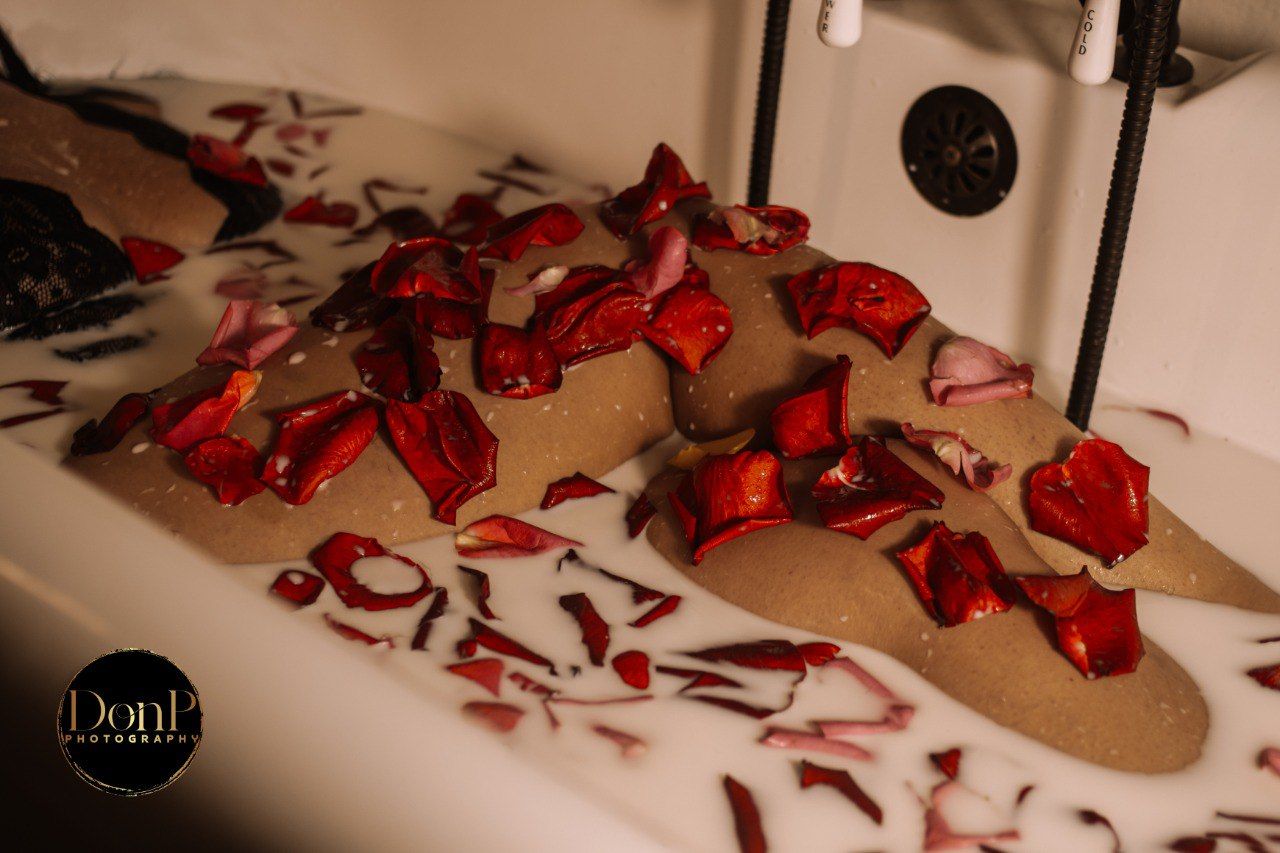 Moody artistic photograph of a body resting in a milk bath with red rose petals, exploring intimacy, vulnerability, and sensual storytelling
