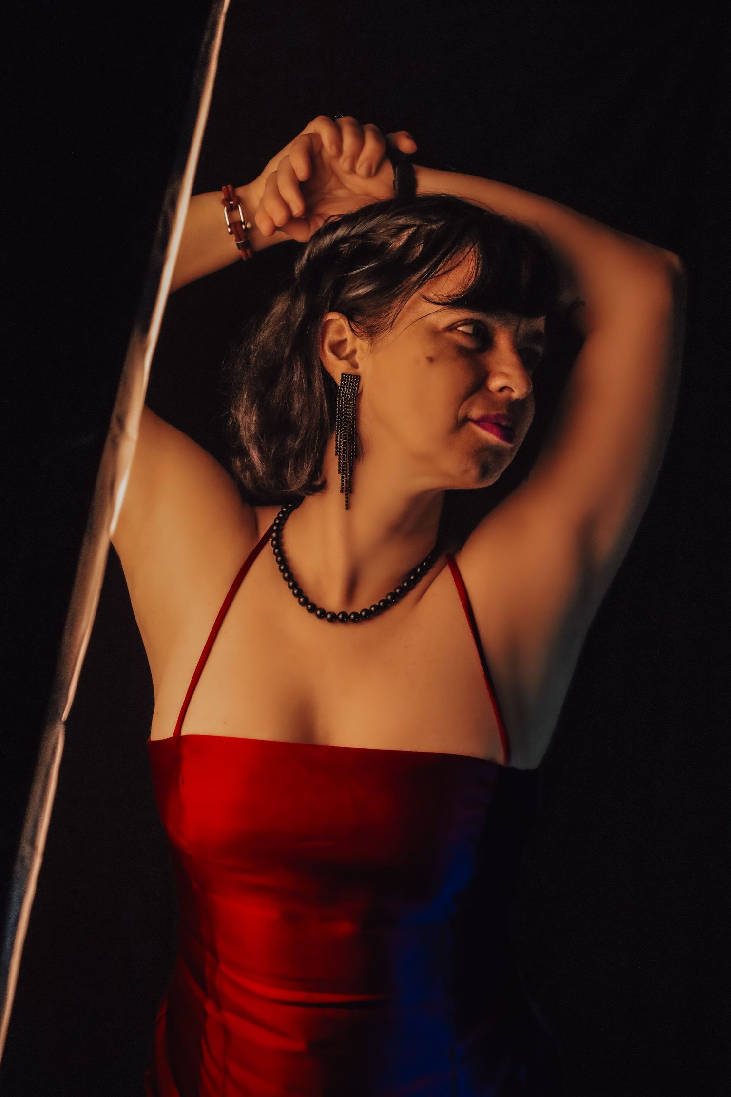 Cinematic portrait of a woman in a red dress with arms raised, captured in warm light, expressing confidence, movement, and embodied presenc
