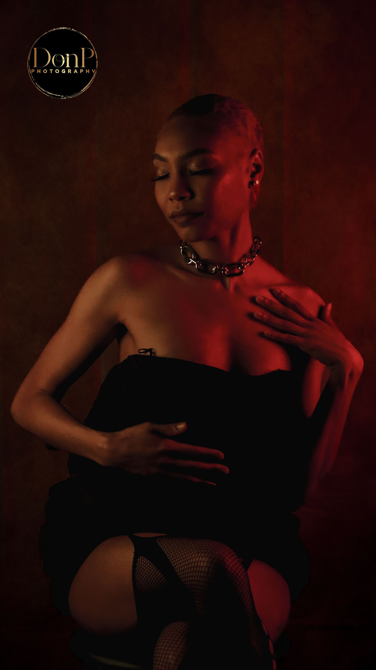 Cinematic boudoir photography portrait of a seated figure in warm red tones, emphasizing confidence and presence.