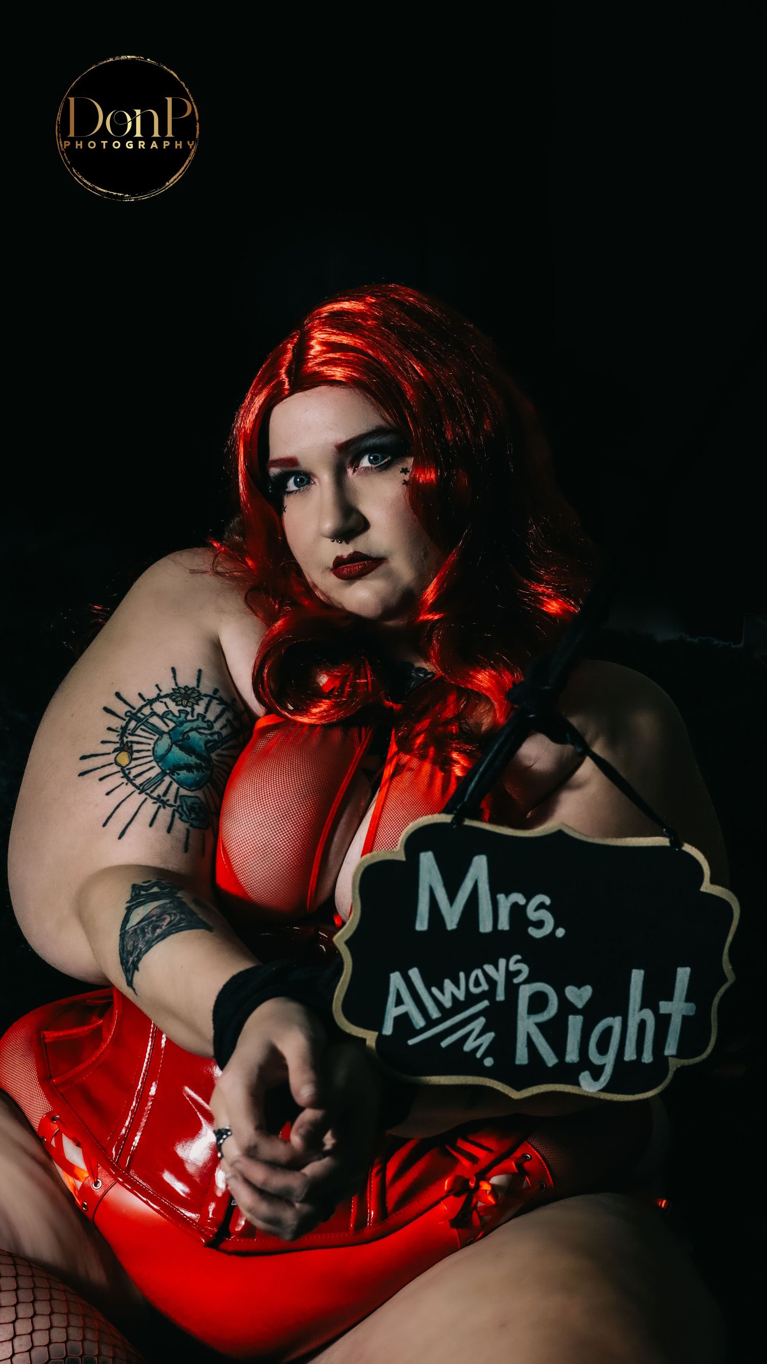 Expressive boudoir photography portrait of a red-haired subject in dramatic light, blending playful messaging with bold, cinematic mood.