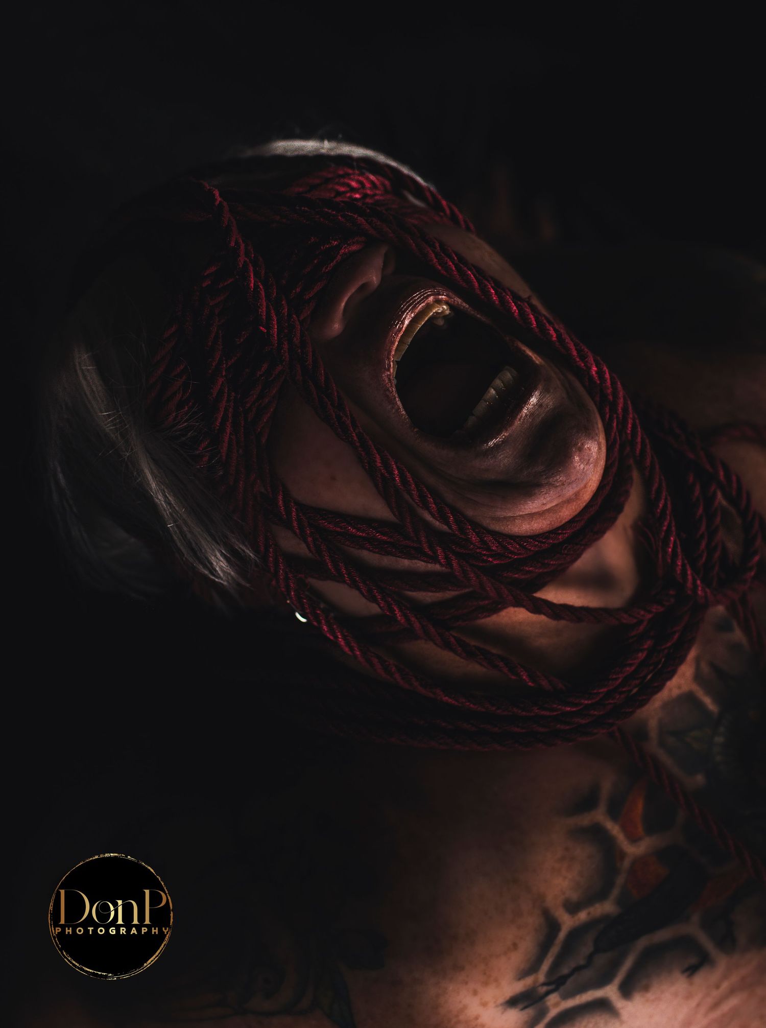 Moody portrait with rope framing the face, exploring vulnerability, power, and shadow boudoir
