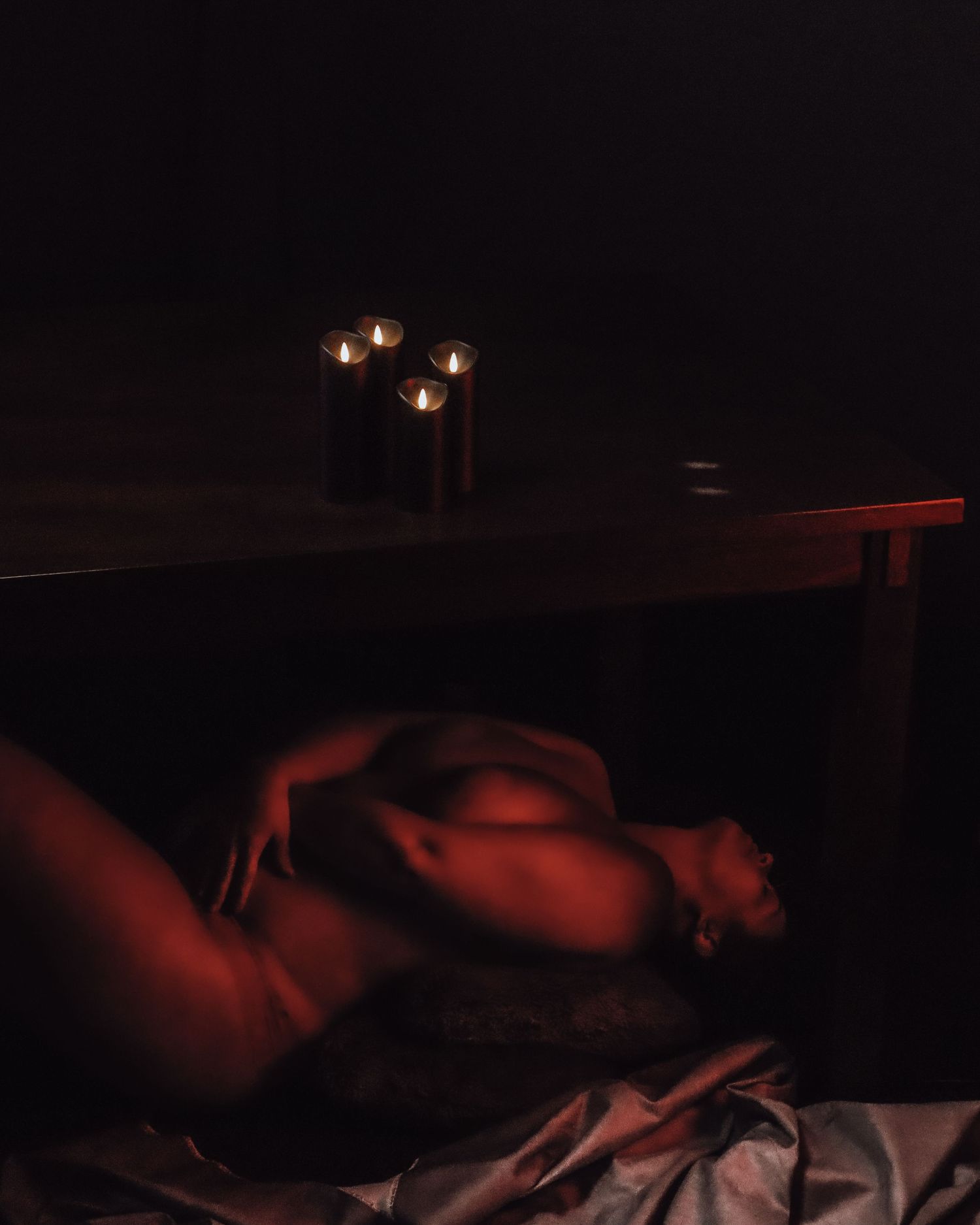 Abstract, candlelit photograph of a reclining body partially obscured by shadow, exploring light, vulnerability, and intimate self-expressio