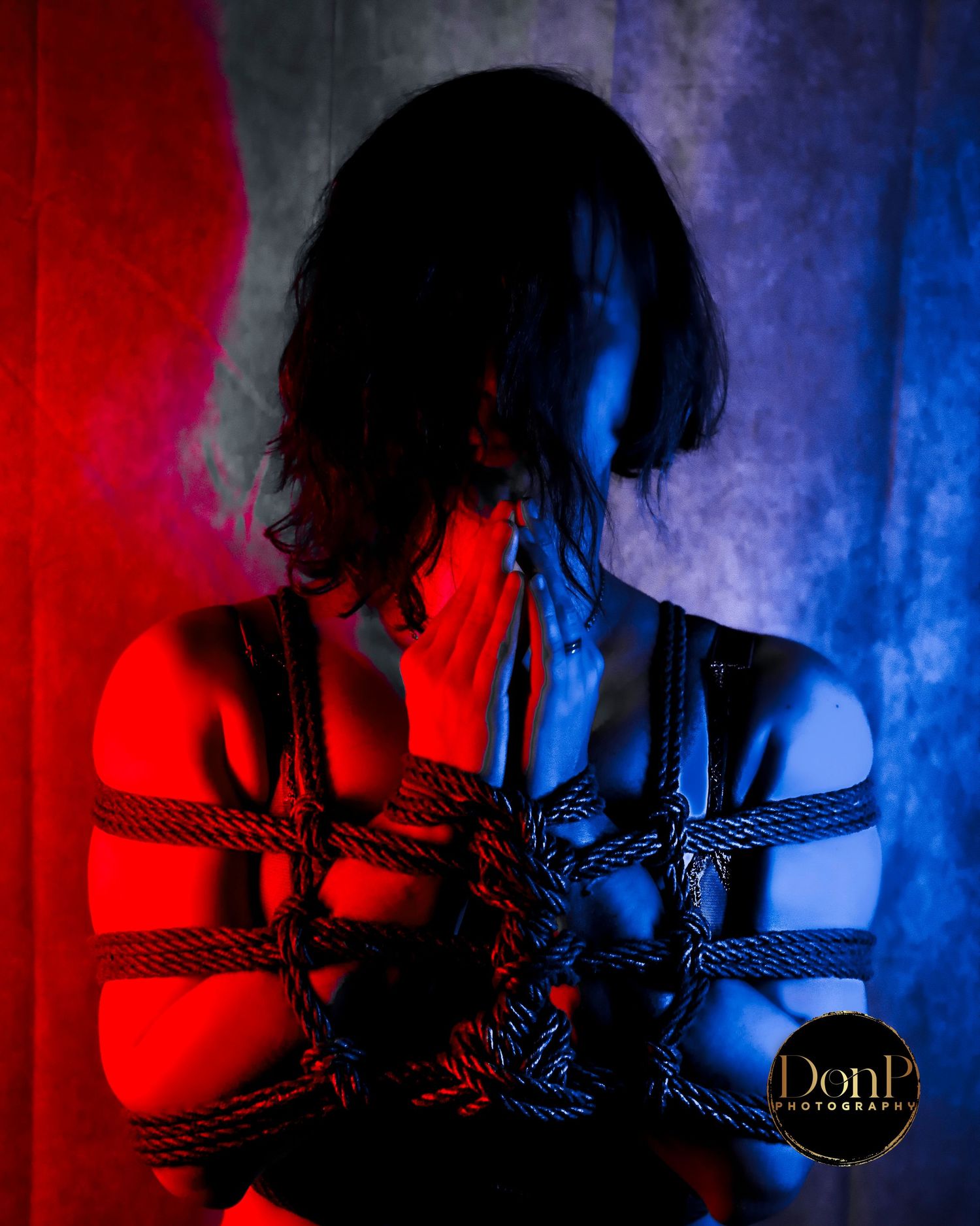 Portrait with dramatic red and blue lighting and rope restraint, expressing emotional intensity and power exchange boudoir