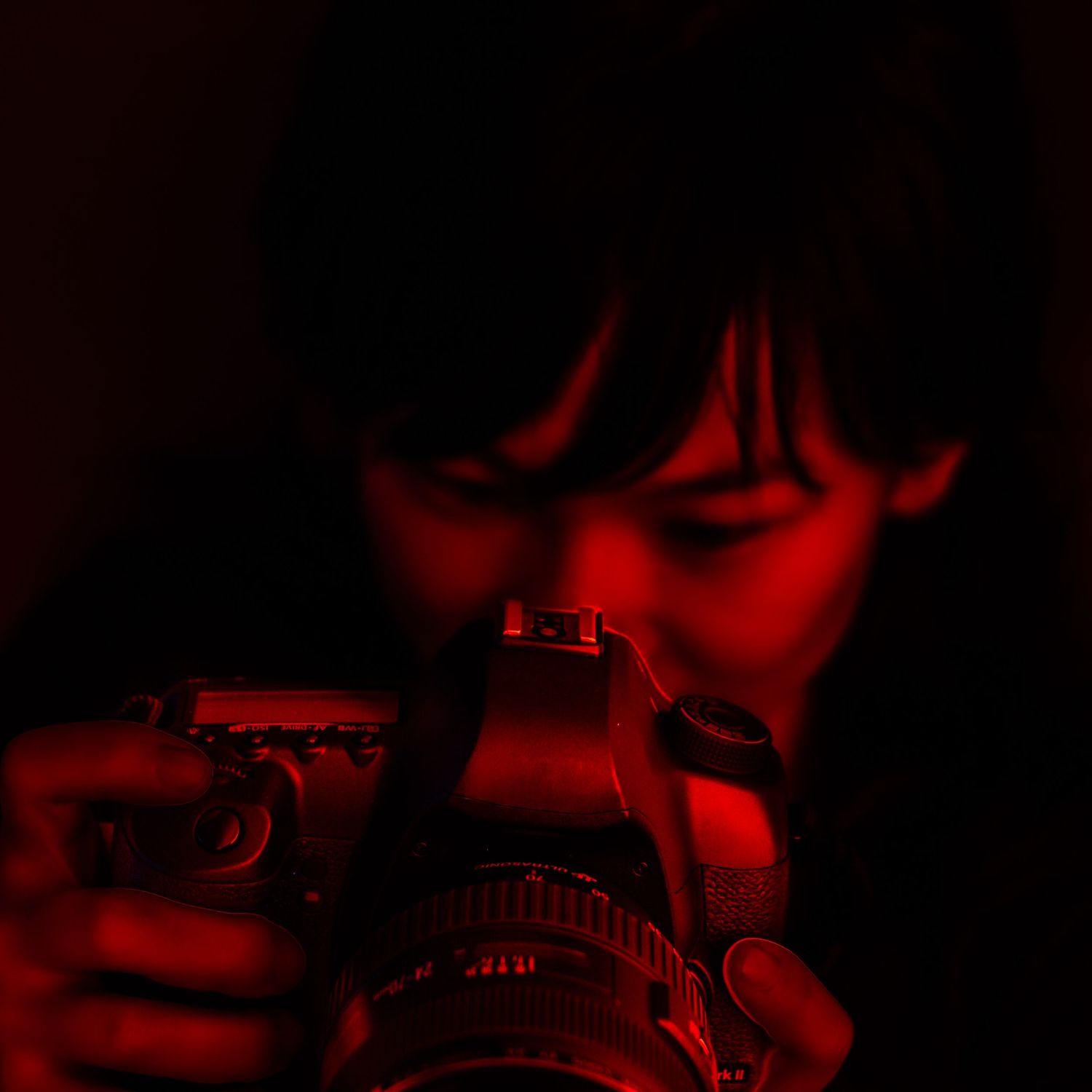 Moody portrait of a photographer holding a camera in red light, symbolizing creative focus, vulnerability, and the act of seeing through an