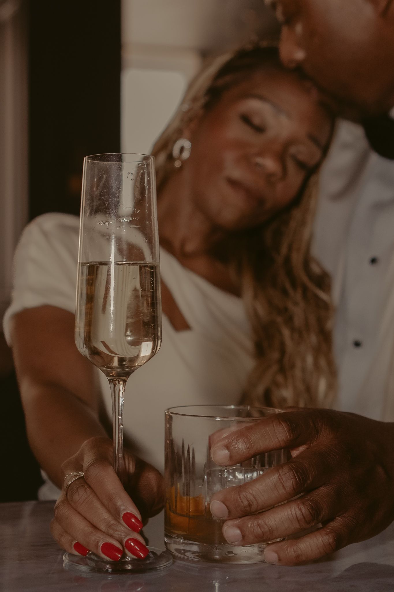 Couple sharing a romantic moment with champagne flute and whiskey glass on a marble surface.