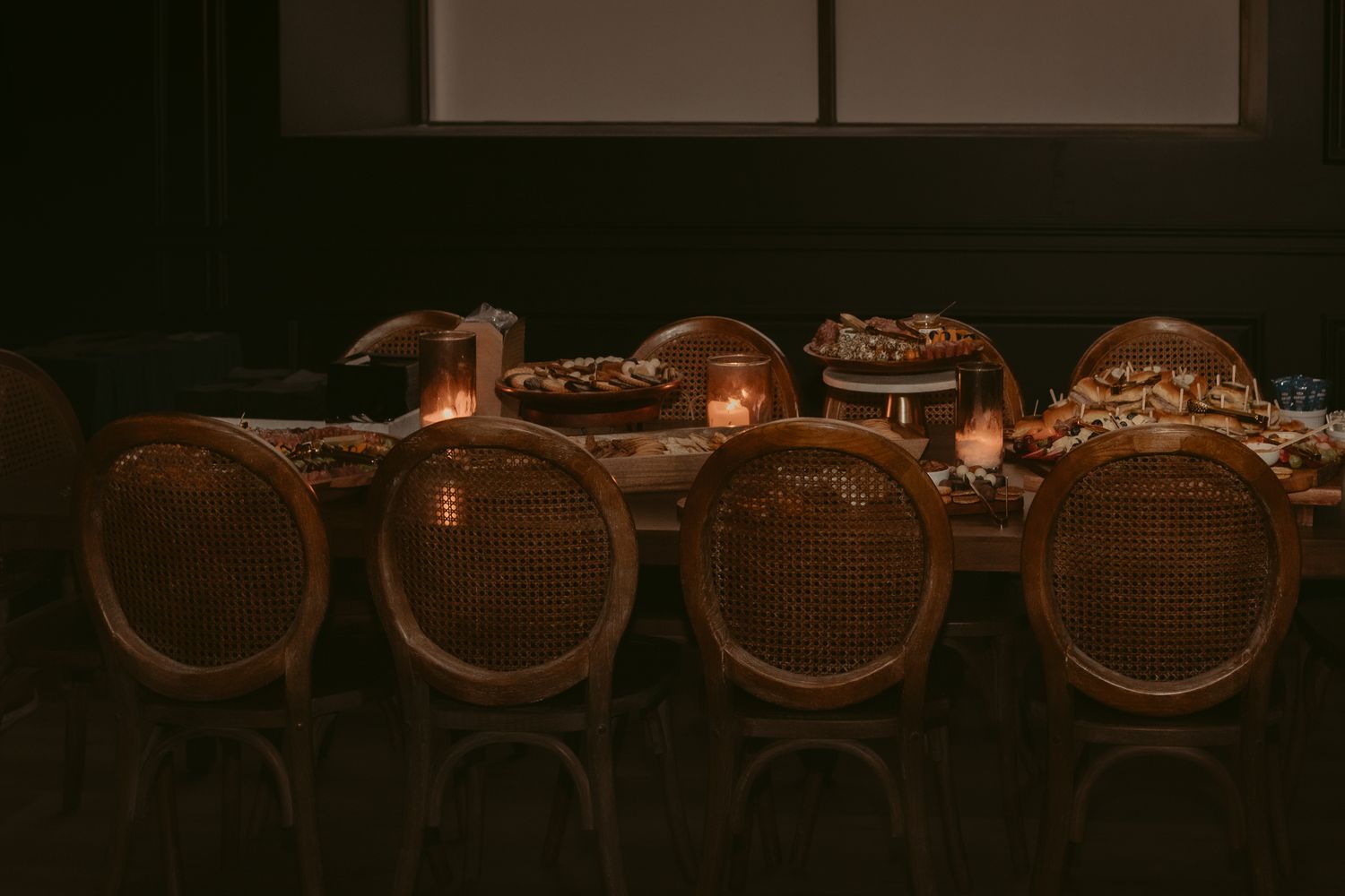 Dimly lit elegant wedding reception table with rattan chairs and warm candlelight ambiance.