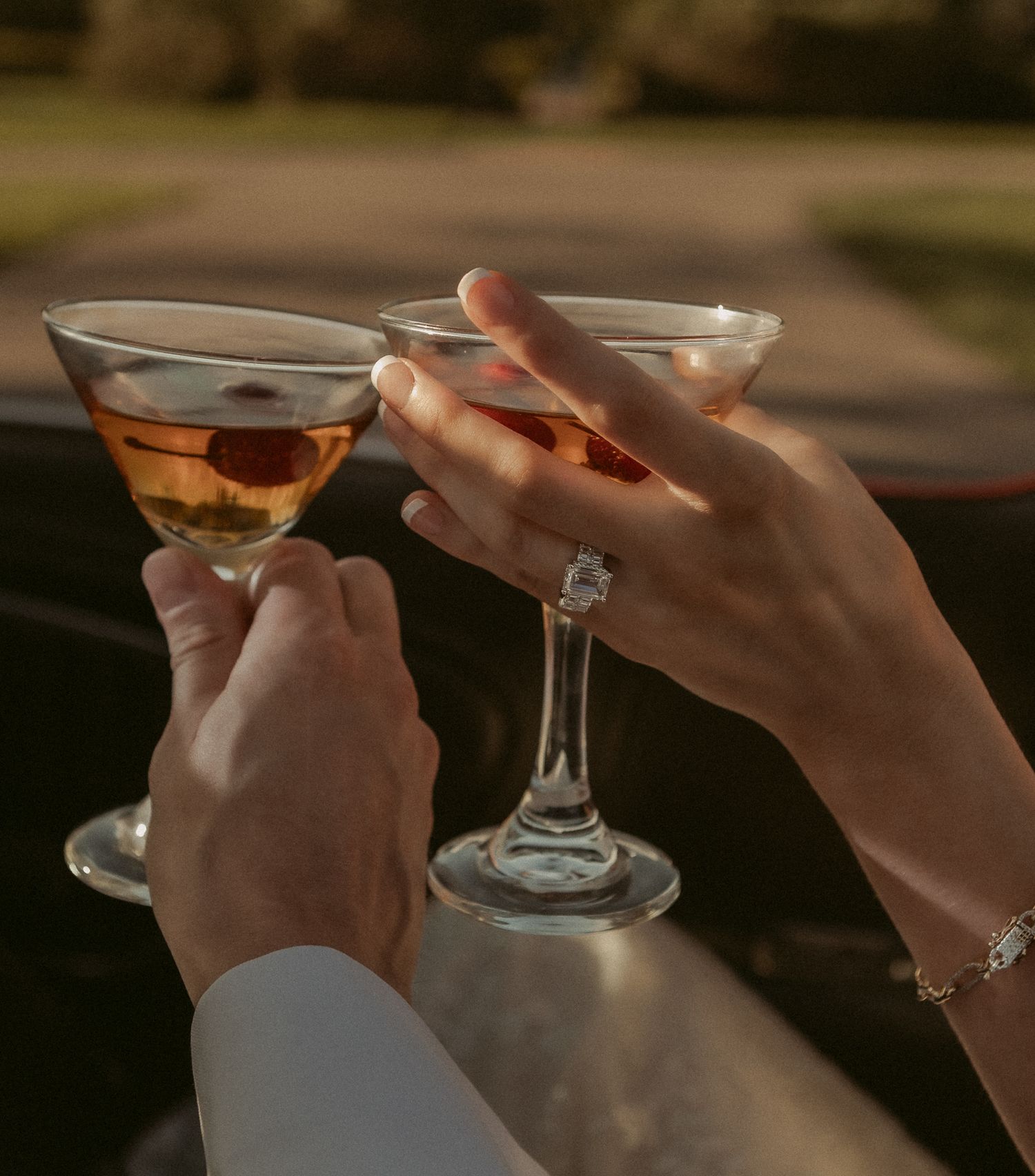 Bride and groom clink martini glasses with cherries, bride wearing diamond engagement ring.