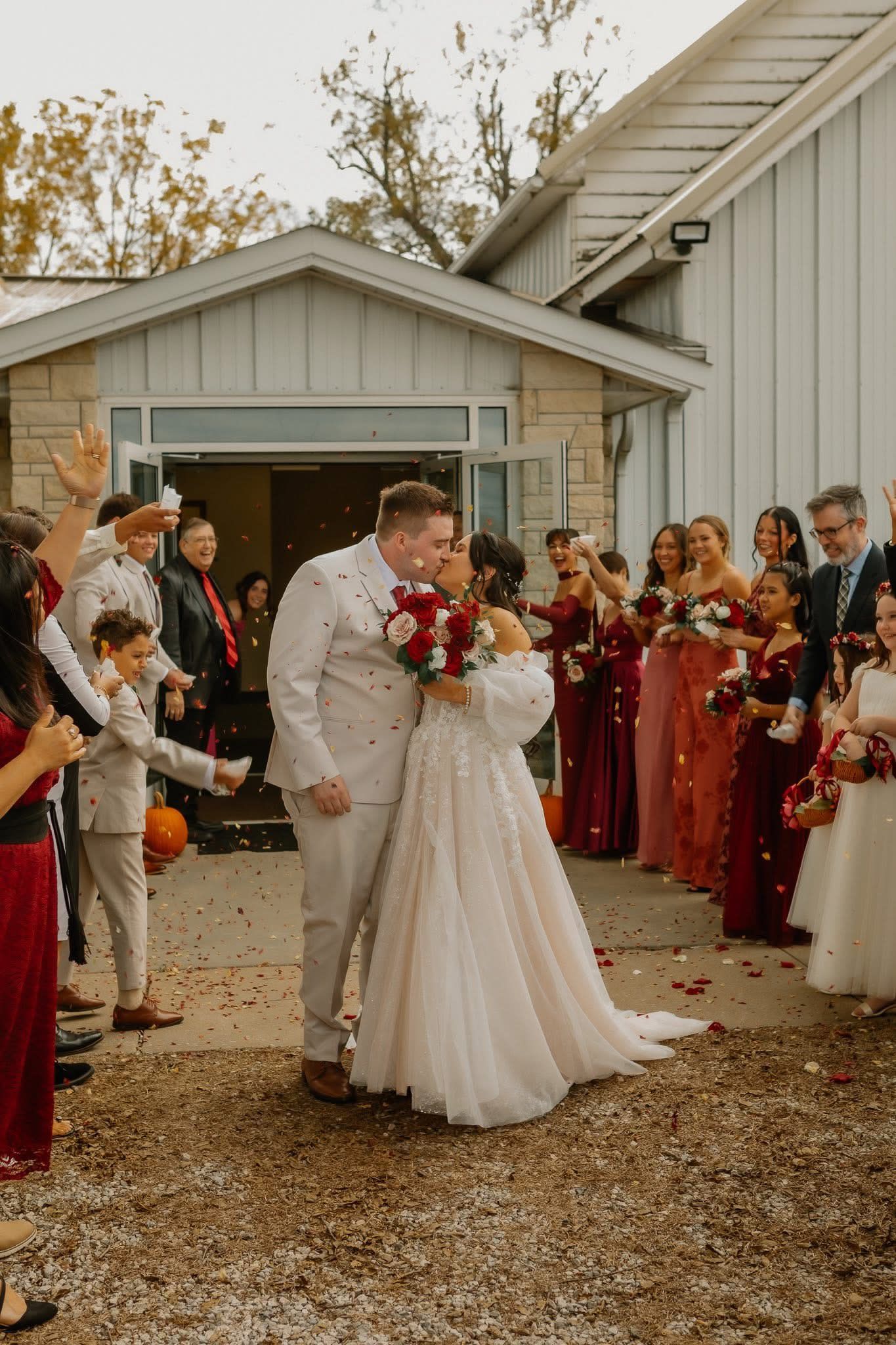 Bride and groom share joyful kiss during confetti send-off with wedding party lining the pathway.