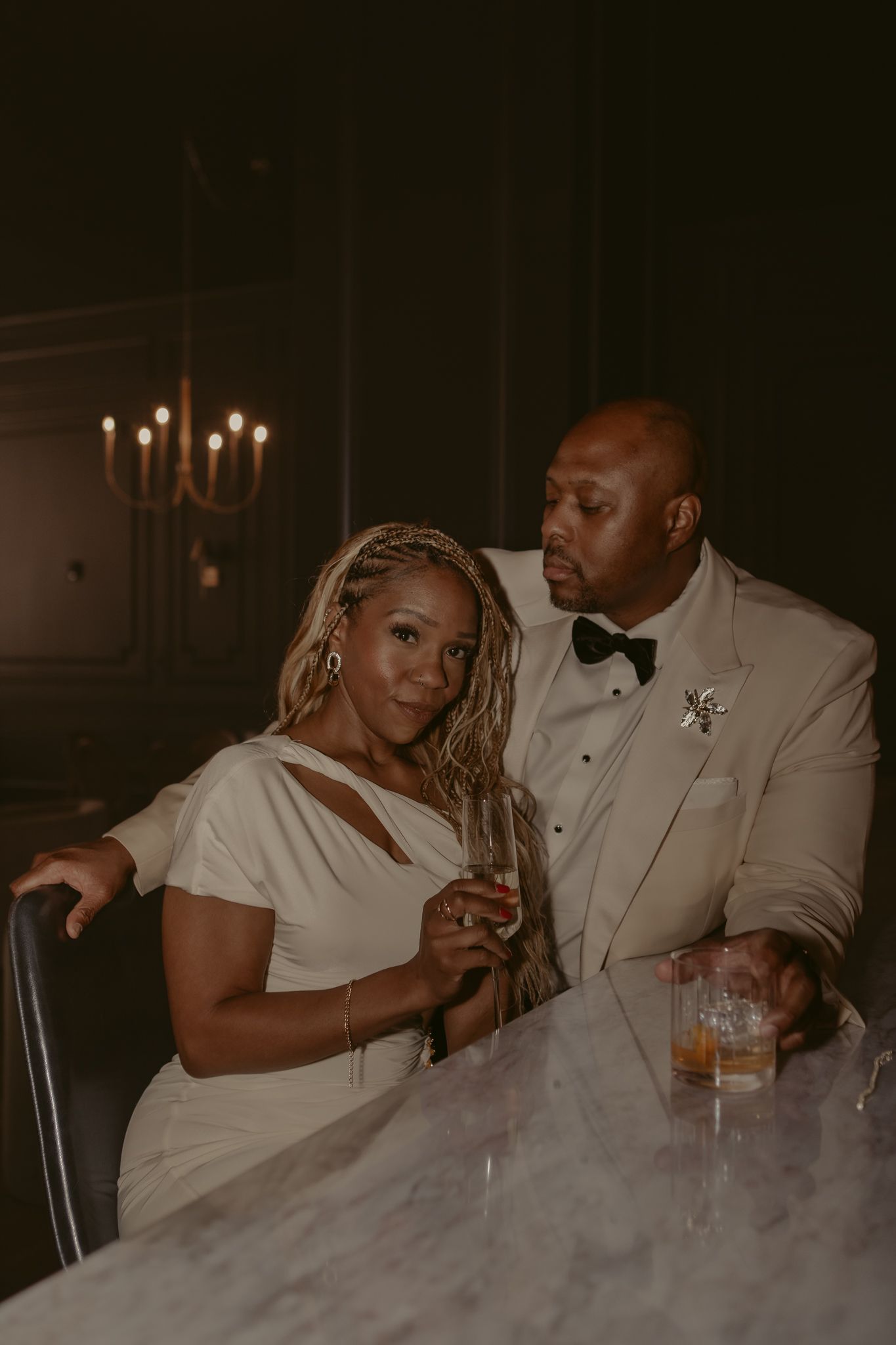 Elegant Black couple in wedding attire sitting at a marble bar with candlelight ambiance.