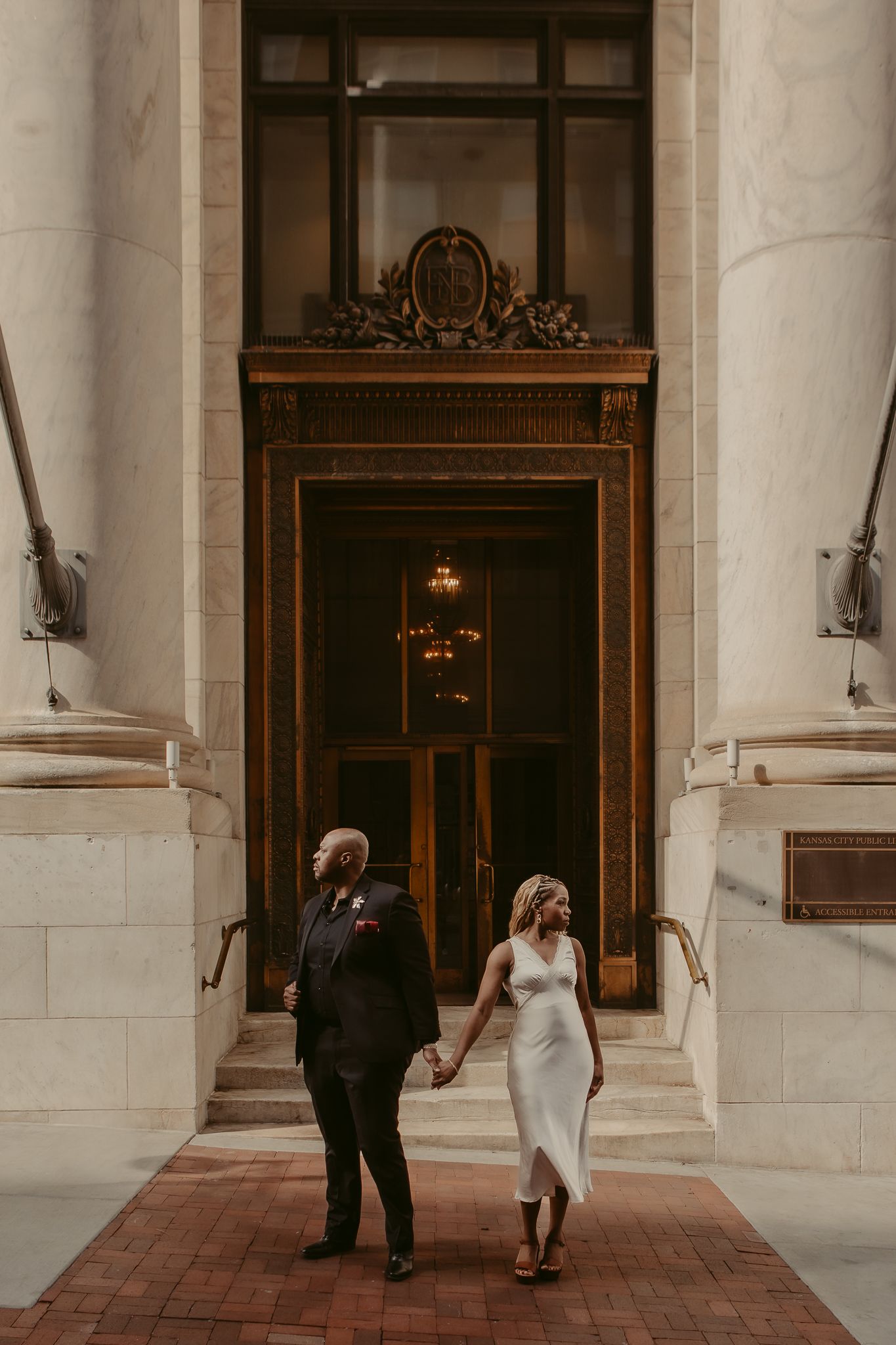 Wedding couple holding hands before grand ornate bronze doors of historic building.