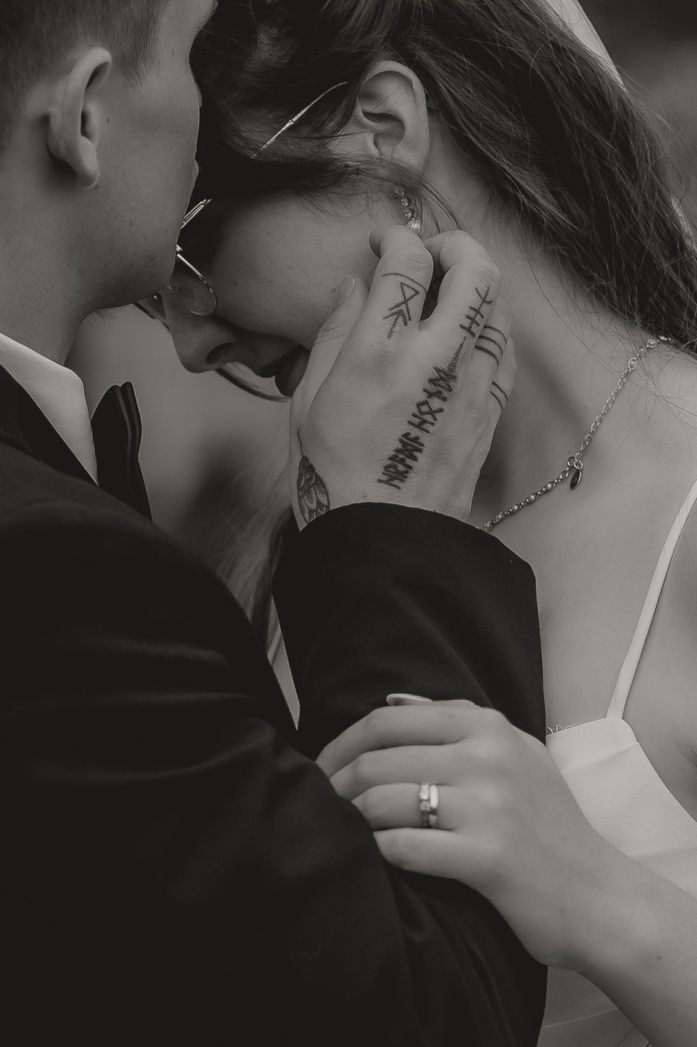 Black and white close-up of tattooed groom tenderly cradling brides face.