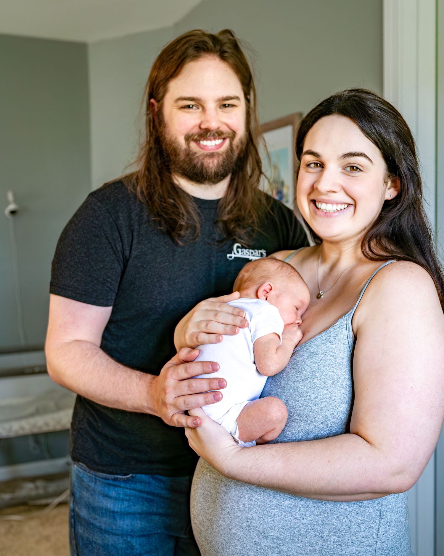 A family of three snuggles together while holding their newborn baby in a casual home setting.