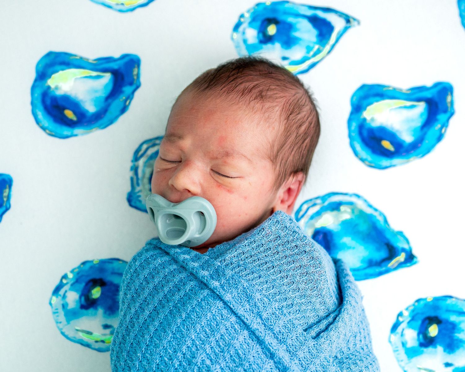 Sleeping newborn swaddled in blue lying on a playful blue watercolor oysters during his lifestyle newborn session.