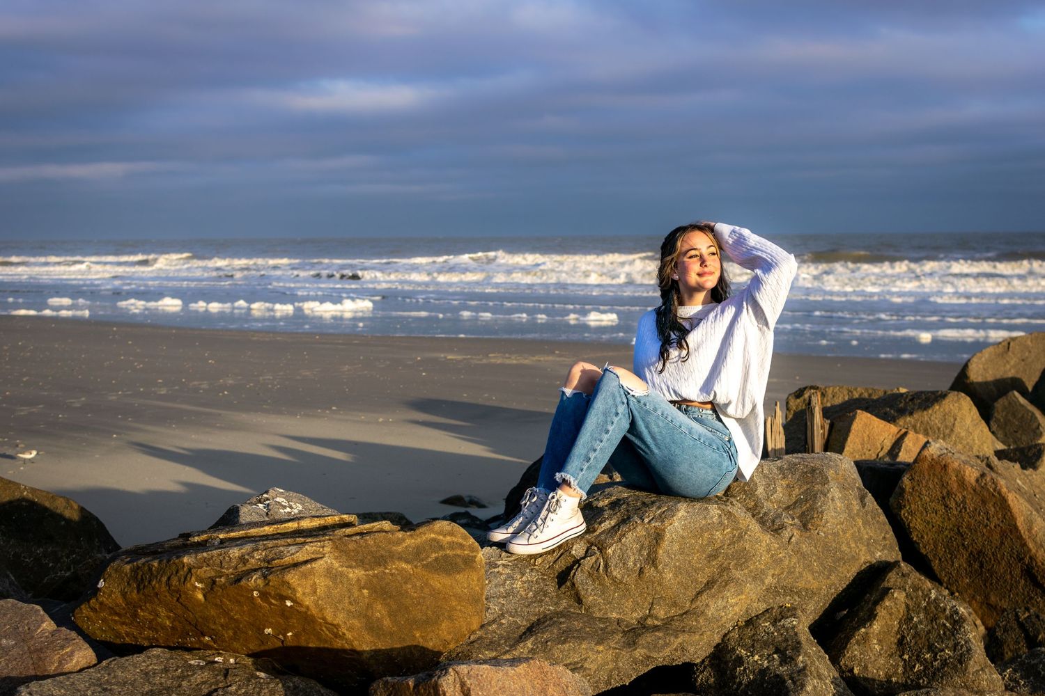 Teenage girl posing on rocks on beach with golden sunlight hitting her face