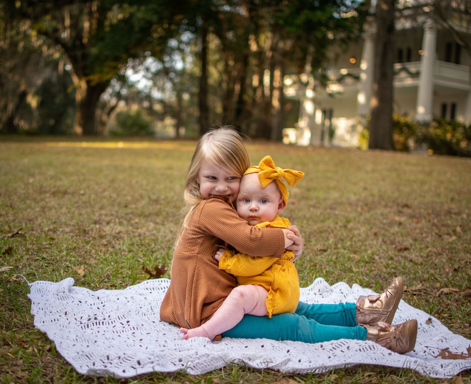 A toddler little girl holds her infant sister in a tight hug