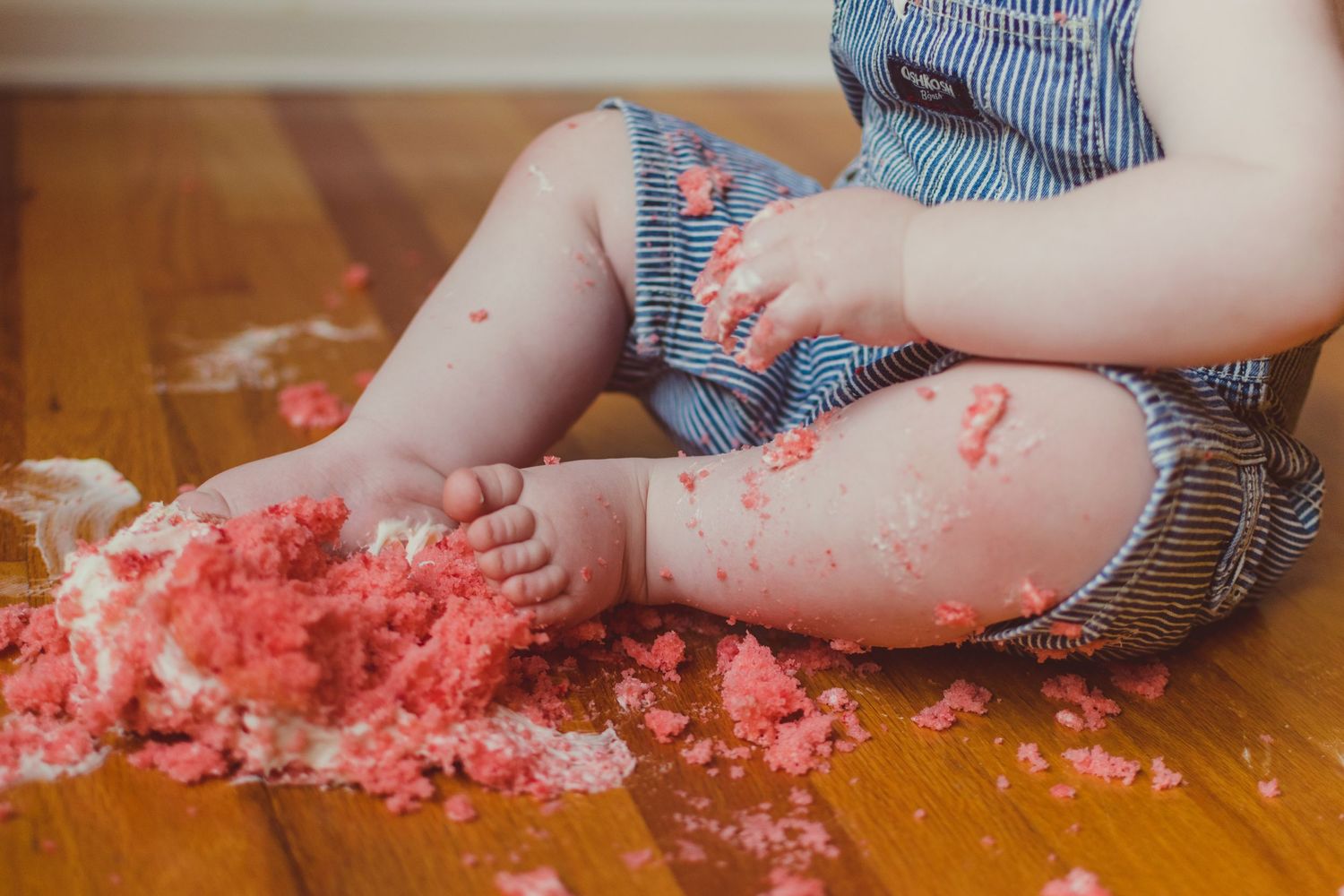 Close up of baby's toes in a smashed strawberry cake on the floor