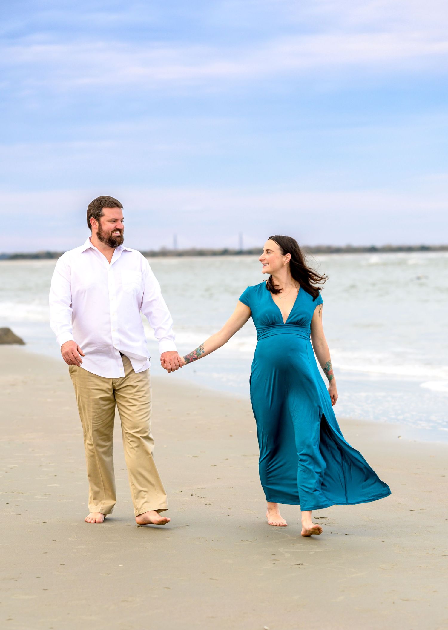 Jasmine and her husband walk hand in hand along the shoreline of Folly Beach during their maternity session