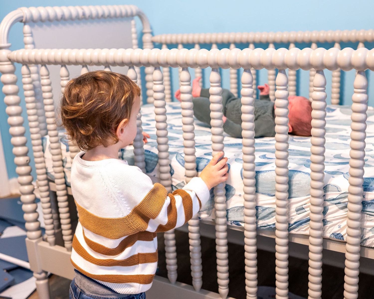 Child reaching for decorative white beaded garland hanging against blue background.