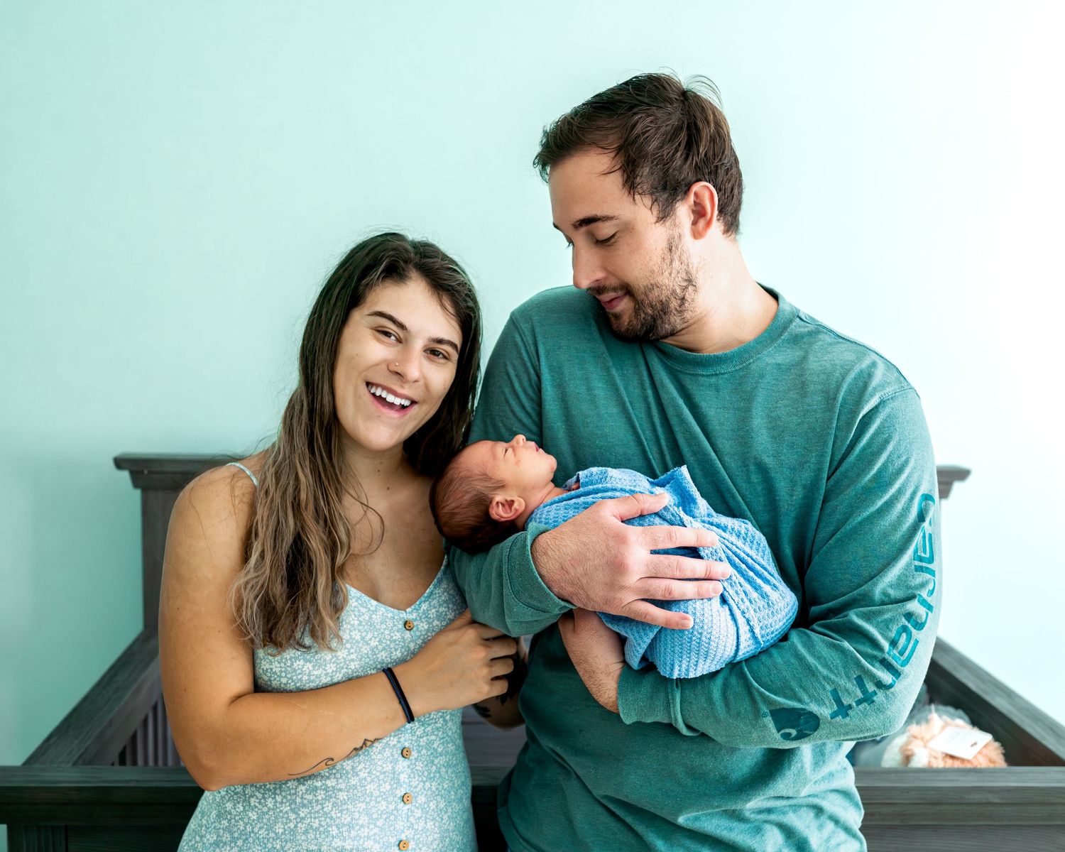Family sharing intimate moments with newborn in mint green nursery setting.