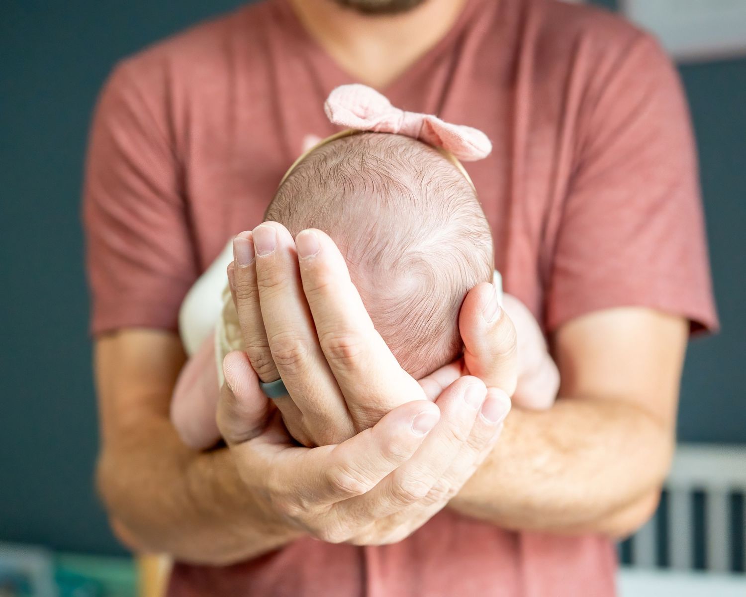 Hands holding newborn baby while wearing coral colored shirt.