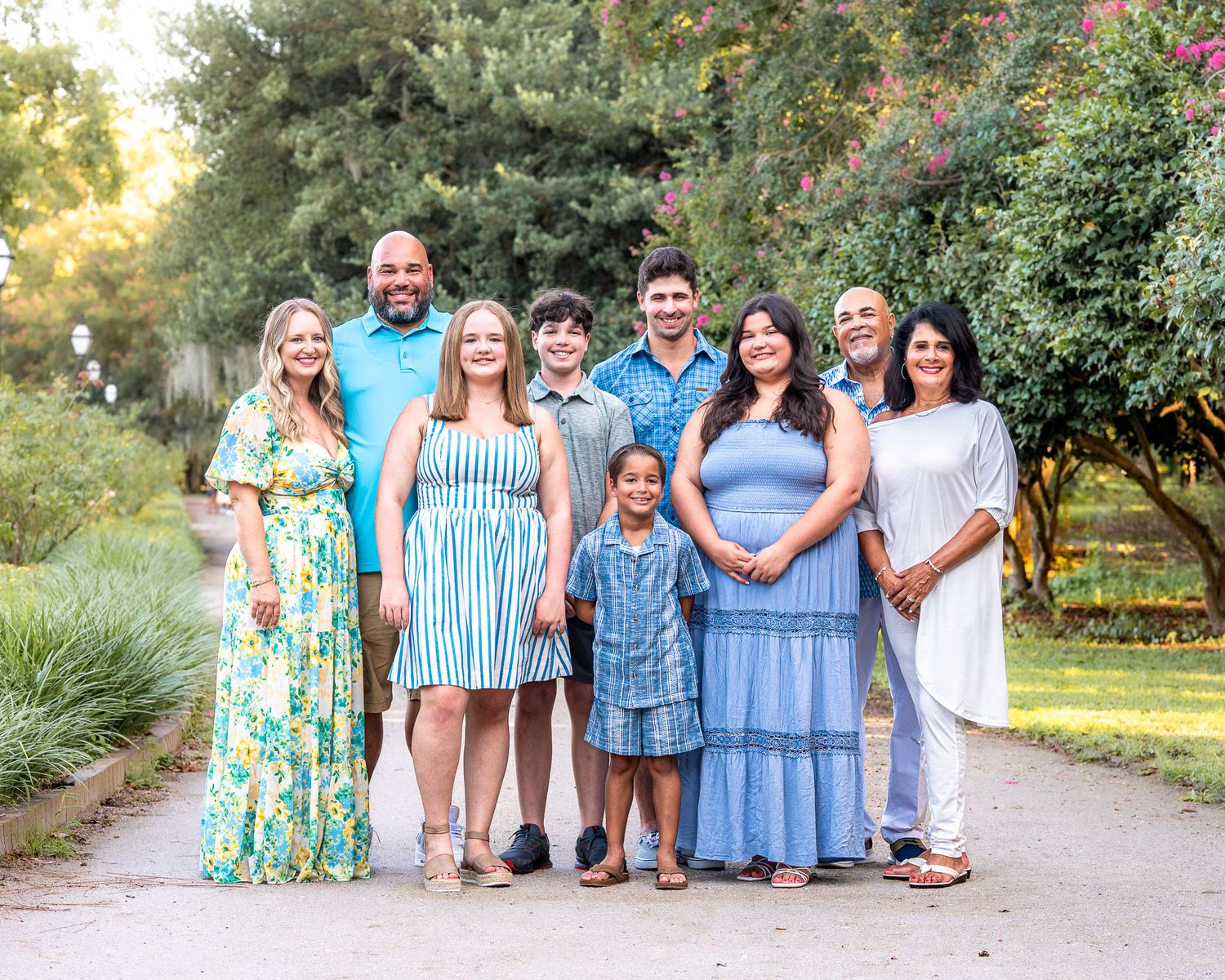 Edited Photo: A group of people wearing coordinated blue and white outfits pose together on a garden path during sunset.