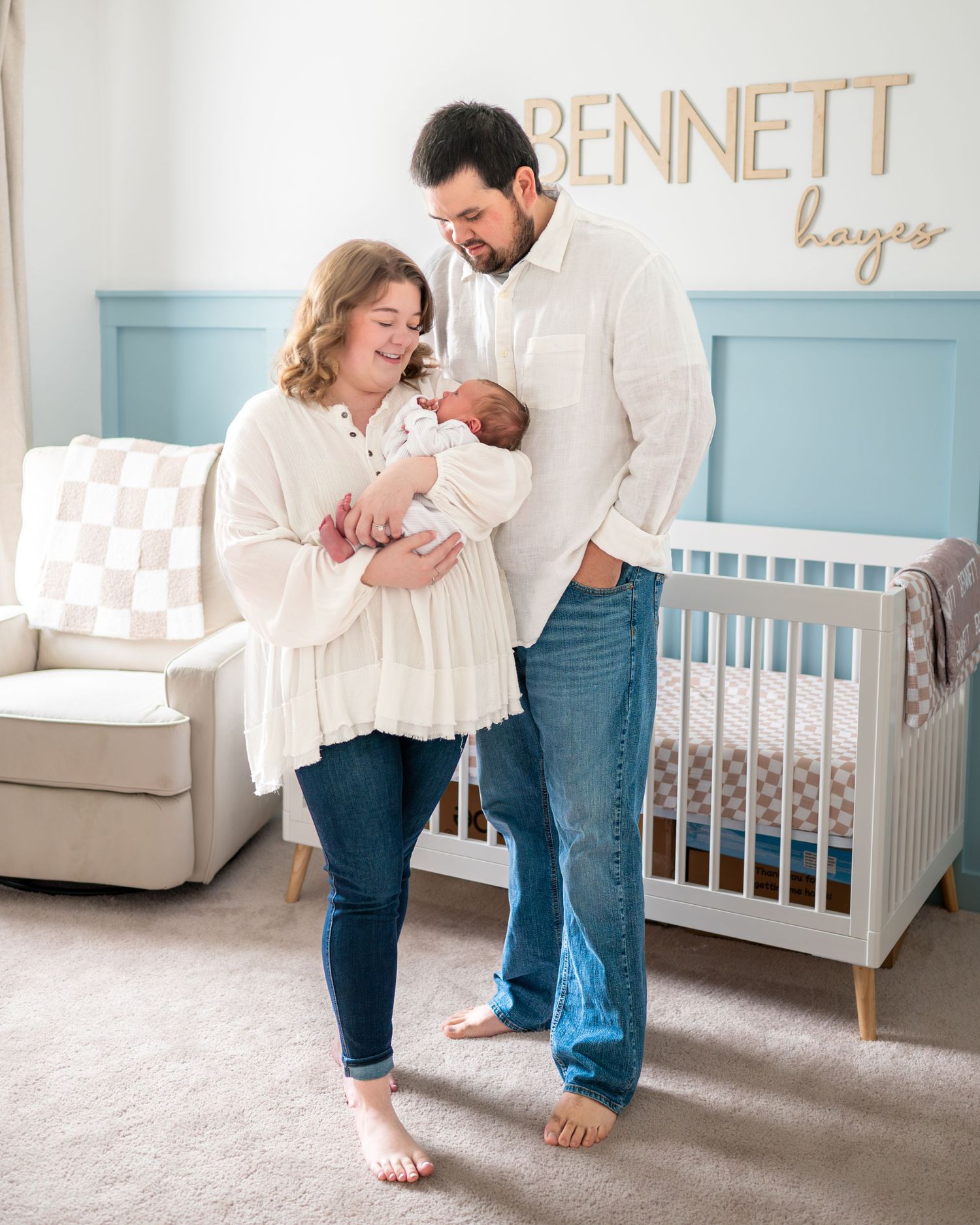Meghan and her husband stand in their nursery holding and looking at their newborn son.