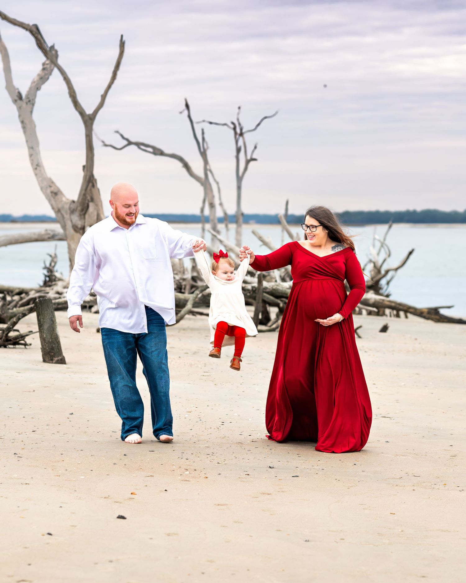 A family shares a joyful moment together on a sandy beach with bare trees and water in the background.
