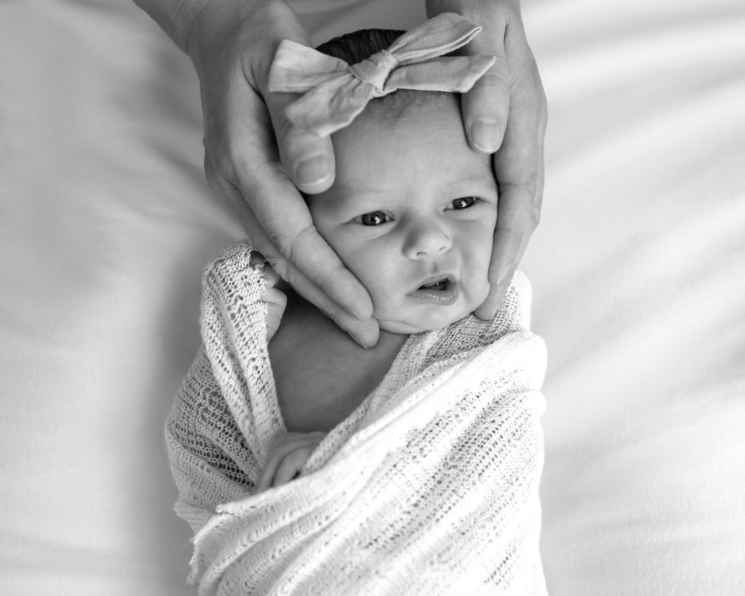 Black and white series of a newborn baby wrapped in soft white blanket.