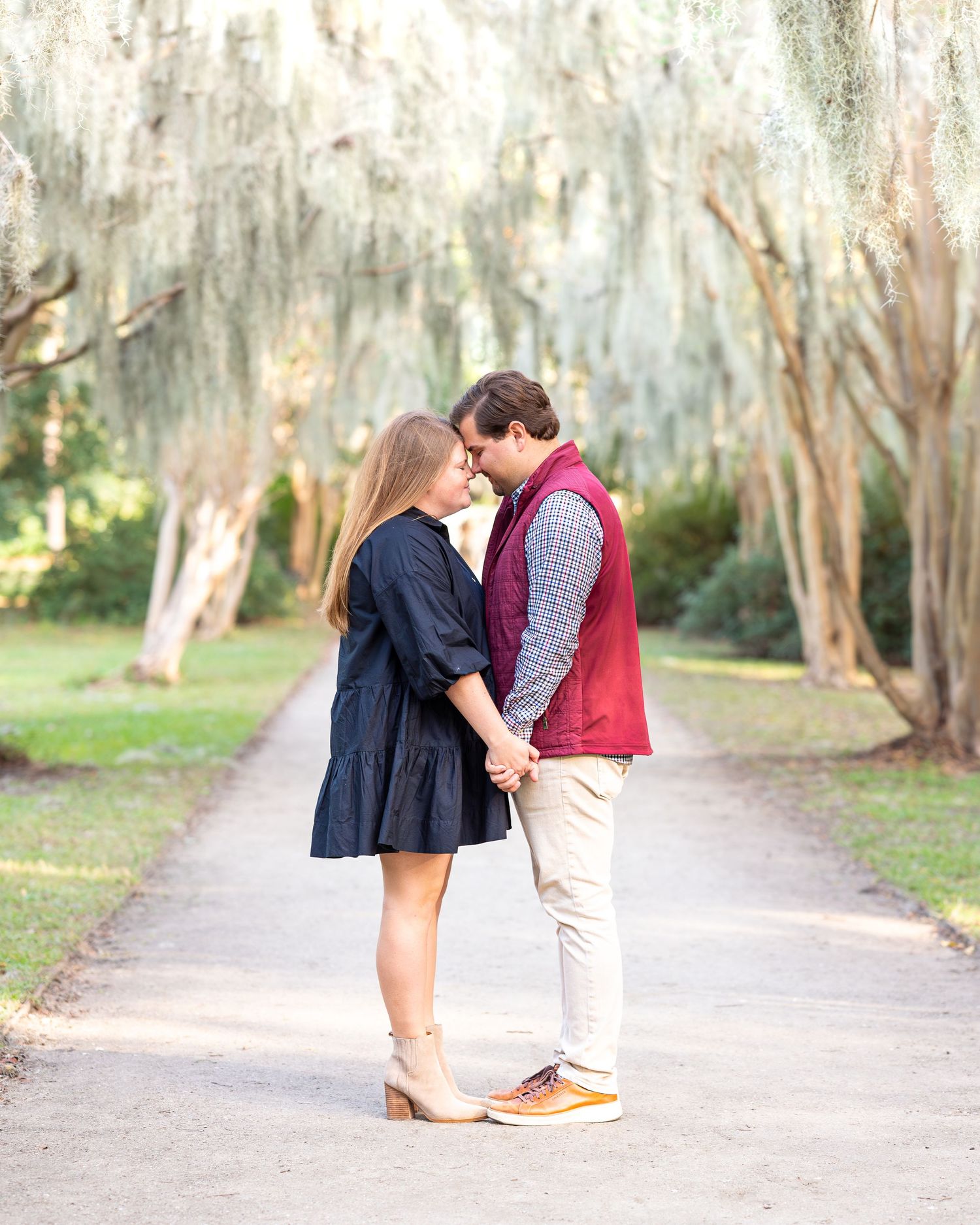 Romantic couple sharing tender moments on a tree-lined path in an outdoor setting.