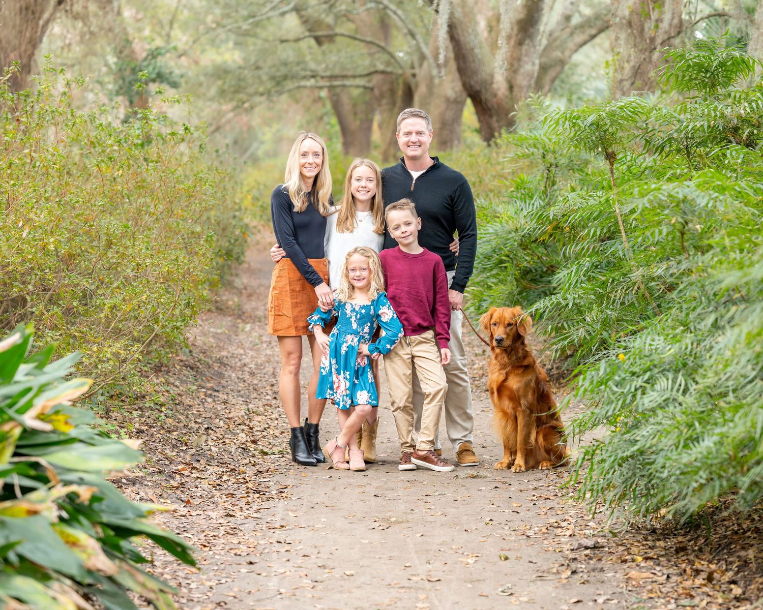 Family walking on a nature trail with a golden retriever dog among Spanish moss trees.