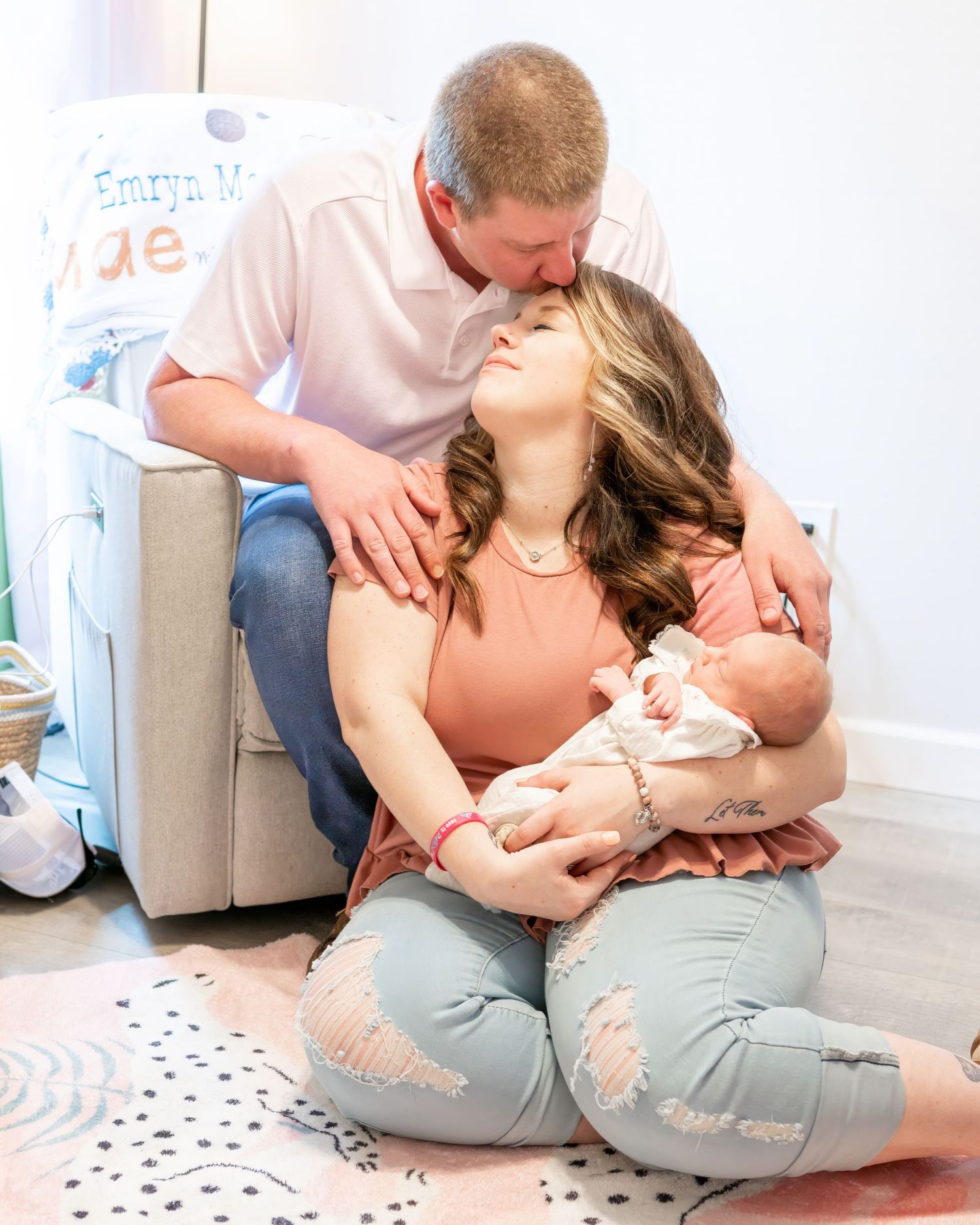 A young mother and father kiss while mom cradles her newborn daughter during their lifestyle newborn session.