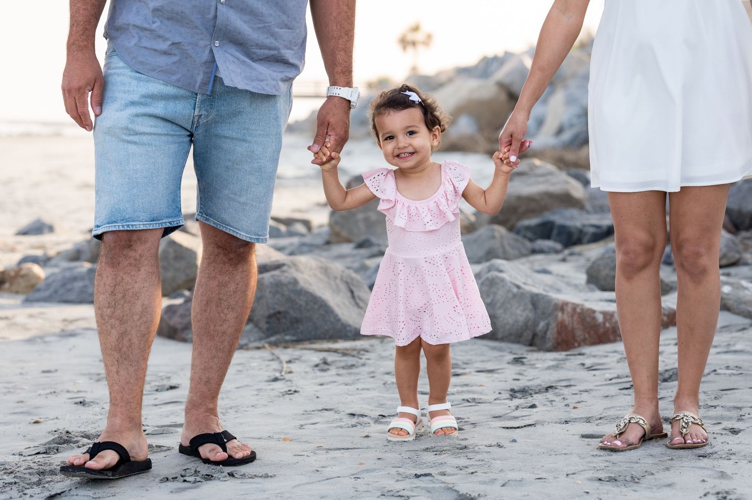 Toddler girl holding onto her parents hands on Folly Beach