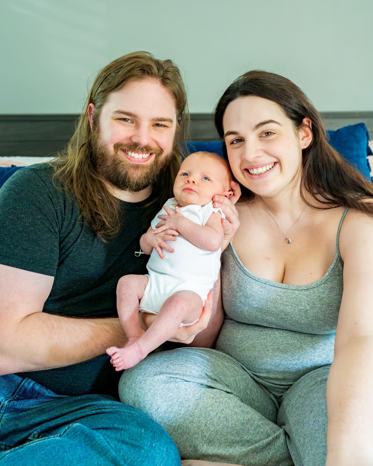 A family sits together on a bed sharing intimate moments with their newborn baby.