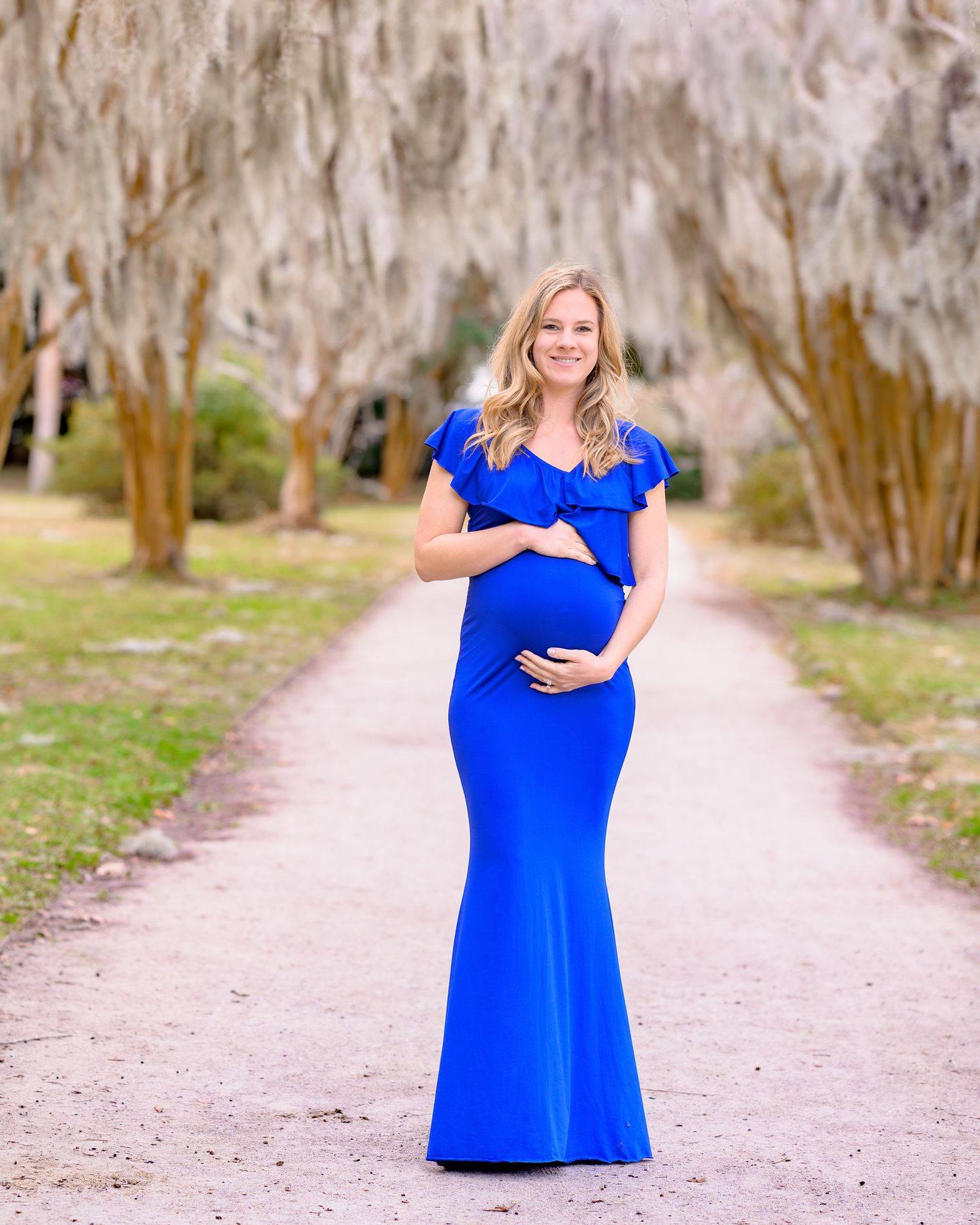 Nicole stands on a path at Hampton Park holding her pregnant belly during her Maternity Session