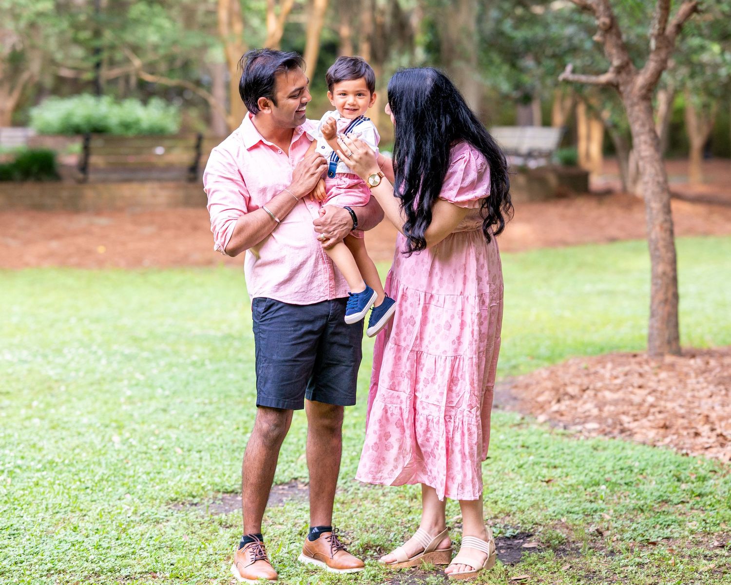 Family sharing intimate moments together in a park setting with trees.