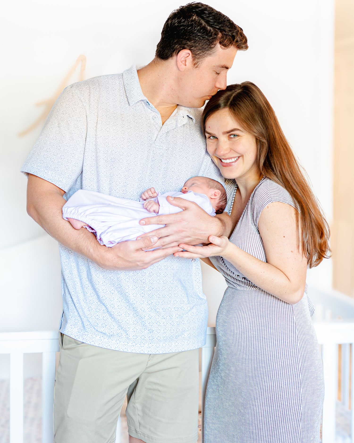 Nathan cradles his newborn daughter as he kisses the top of his wife's head.