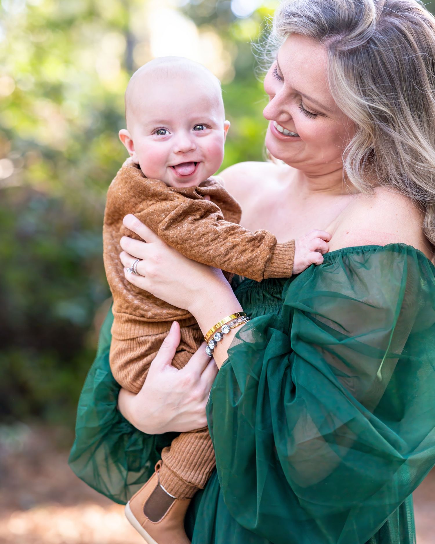 Parent and baby sharing joyful cuddles while wearing green and brown outfits outdoors.