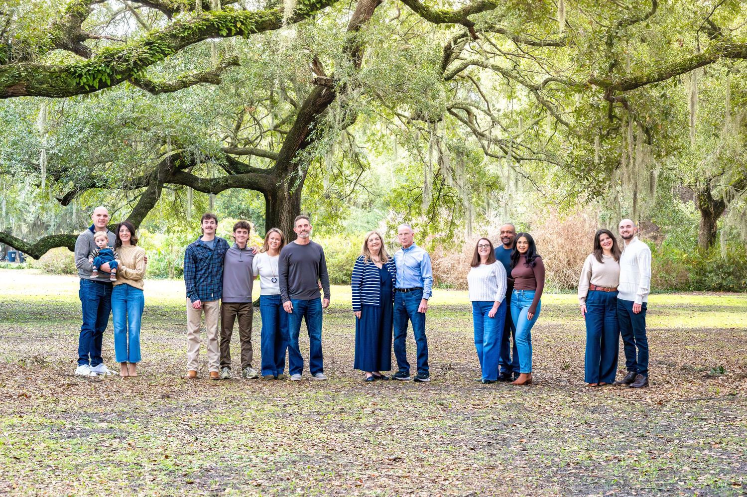 Multiple groups of people pose together under majestic oak trees draped with Spanish moss in a scenic outdoor setting.