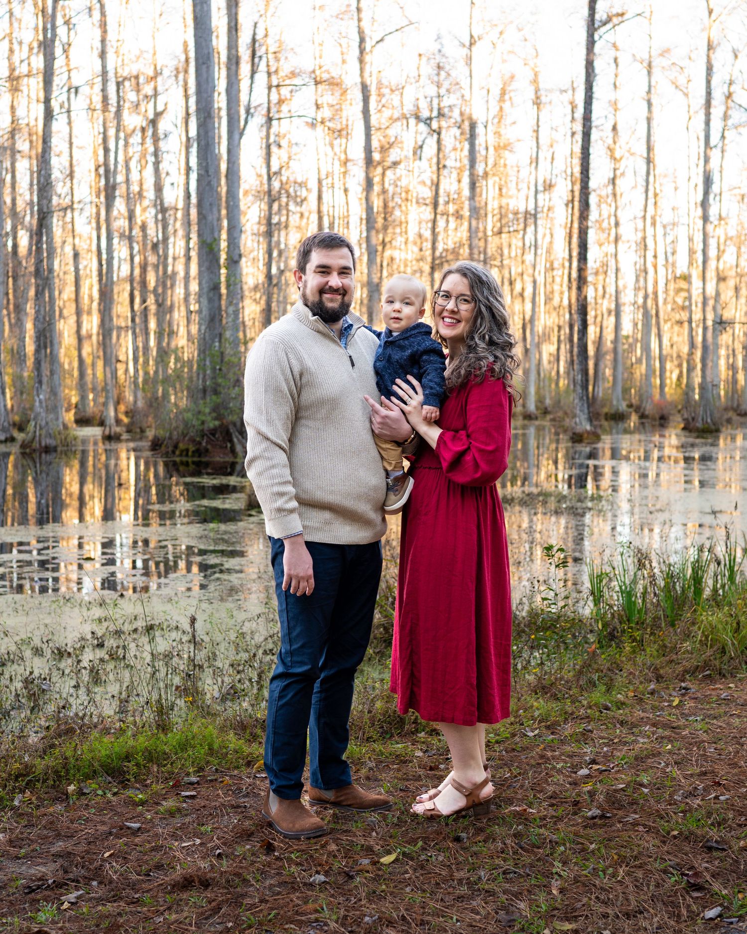 Erin and her husband stand holding their toddler son between them with a swamp view behind them.