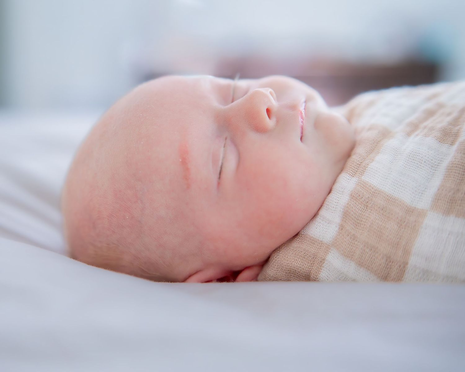 Peaceful sleeping newborn in neutral toned clothing on soft bedding.