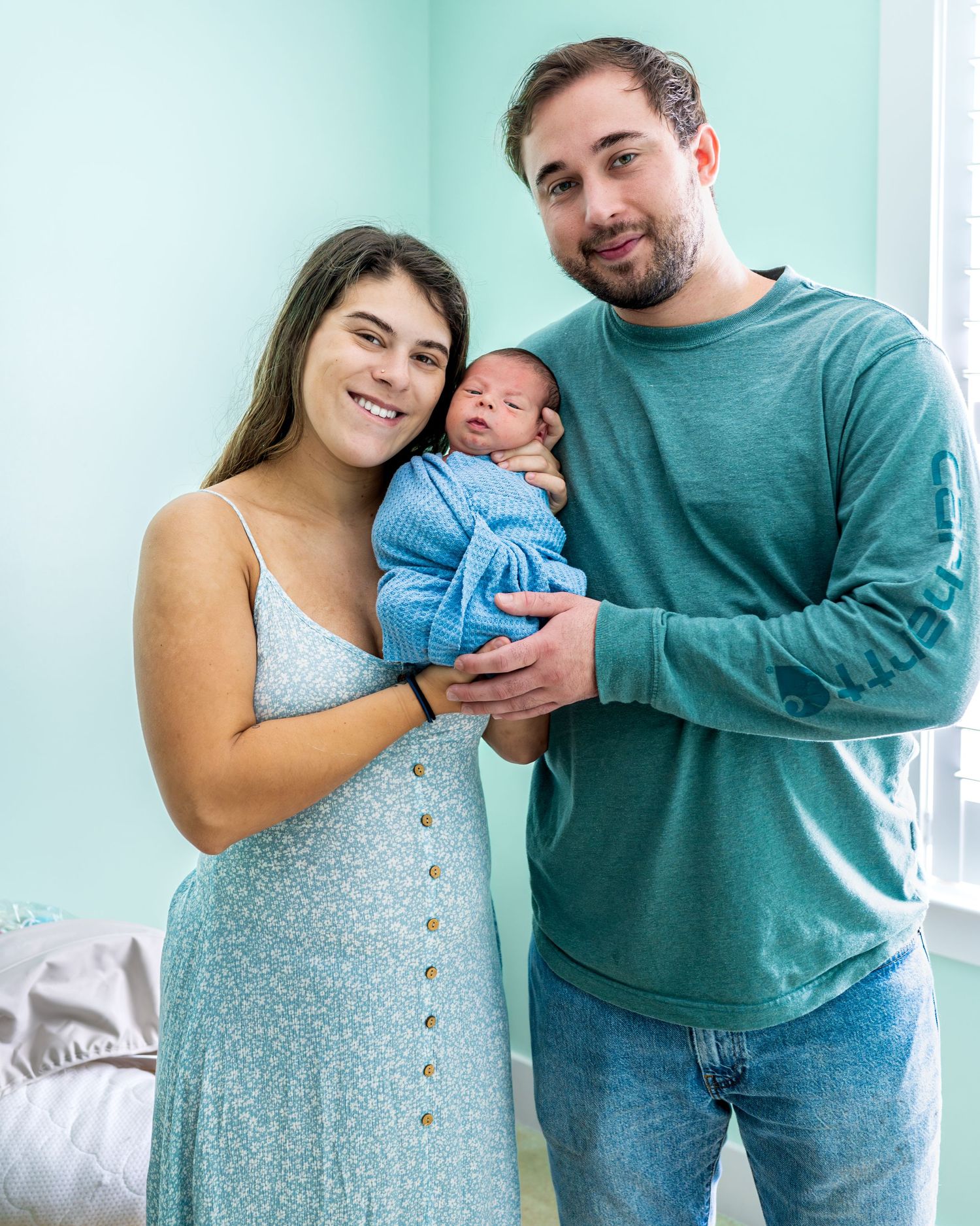 A sweet family moment with their newborn baby dressed in blue against a mint green wall.