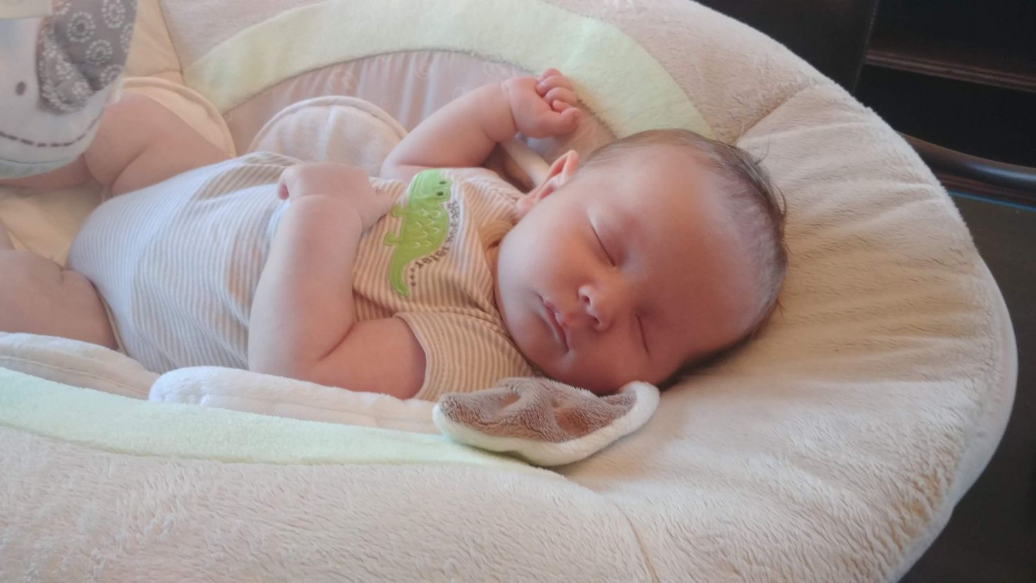 A sleeping baby rests peacefully on a white bouncer.