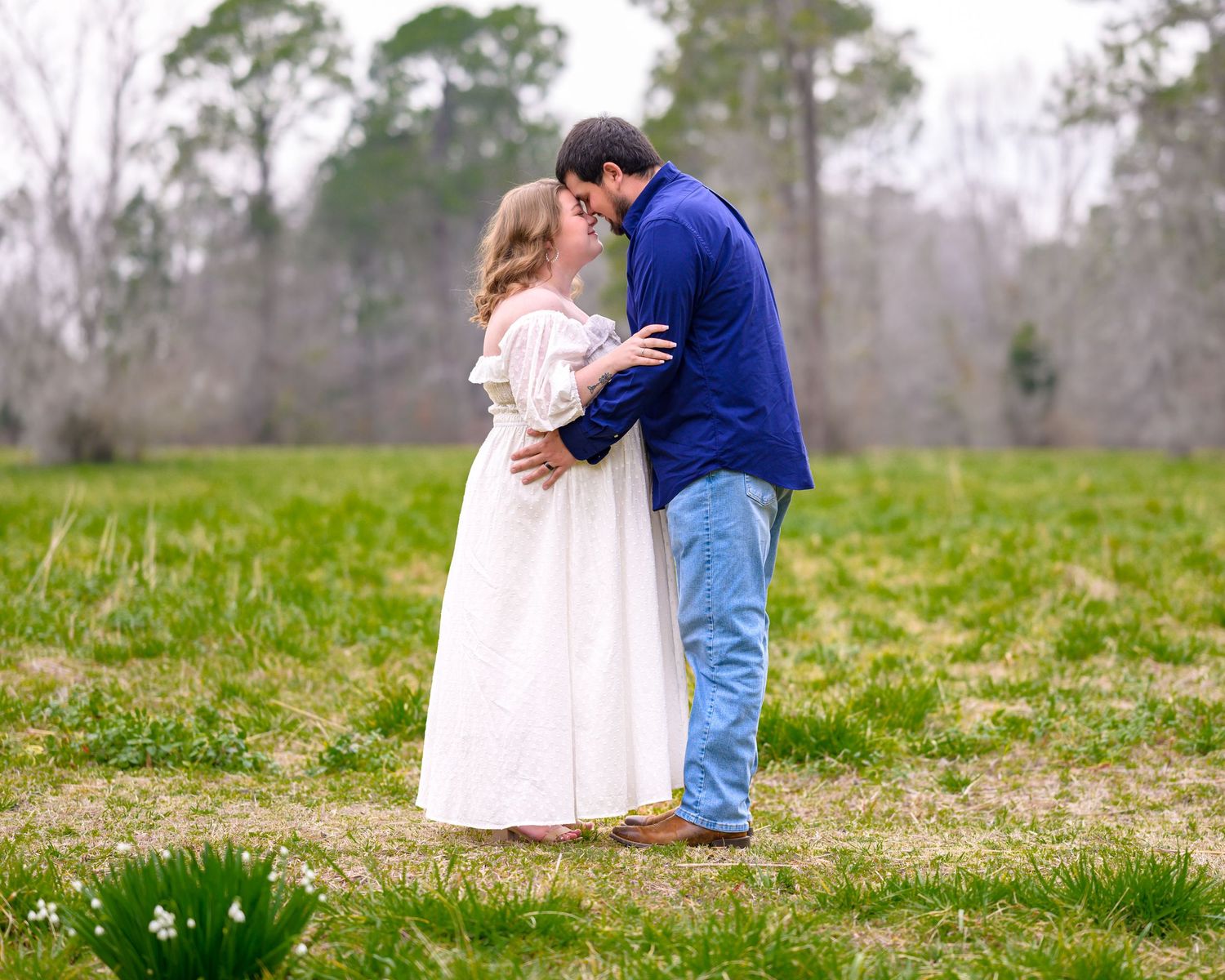 Erin and her husband embrace in a large open field during their maternity session at Strawberry Chapel