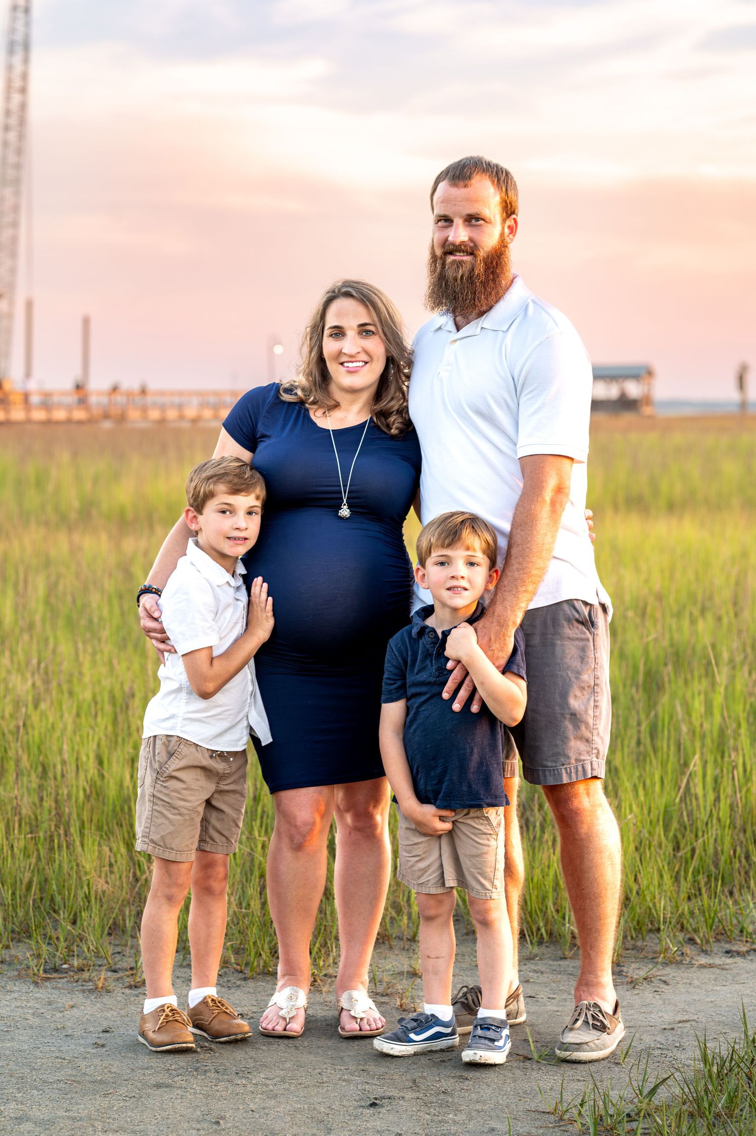 A family of four poses together on a coastal path at sunset with marsh grass in the background.