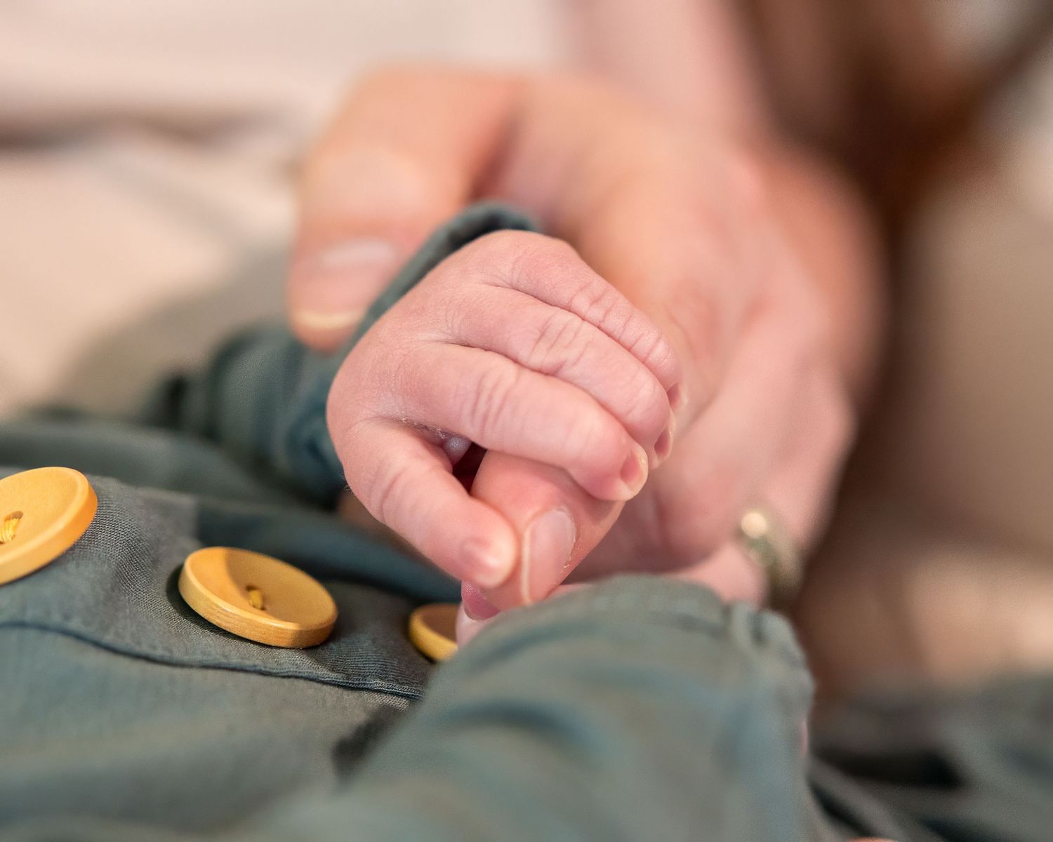 Detail shots of tiny baby hands touching yellow buttons on dark fabric.